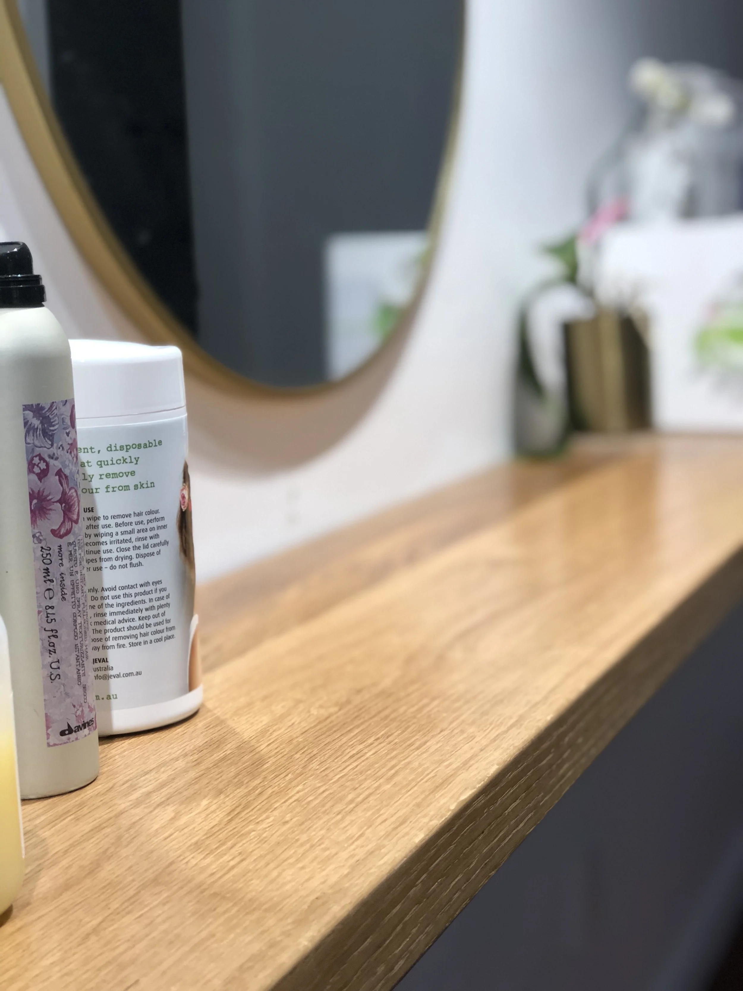 Oak shelving with products displayed and a gold rimmed wall hung mirror on the wall