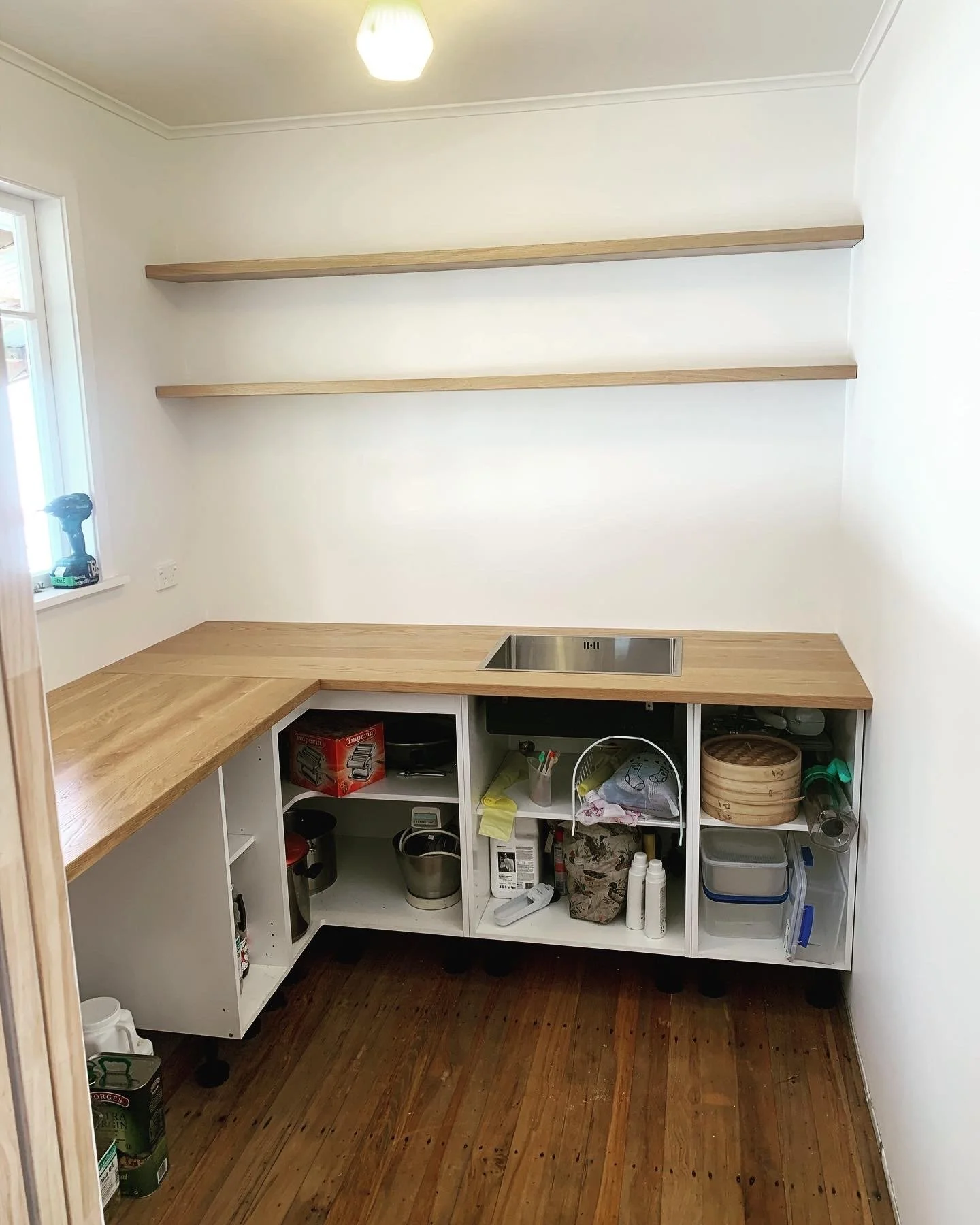 Oak benchtop with stainless steel sink and two oak floating shelves above. Cubby shelving below benchtop with kitchen items 