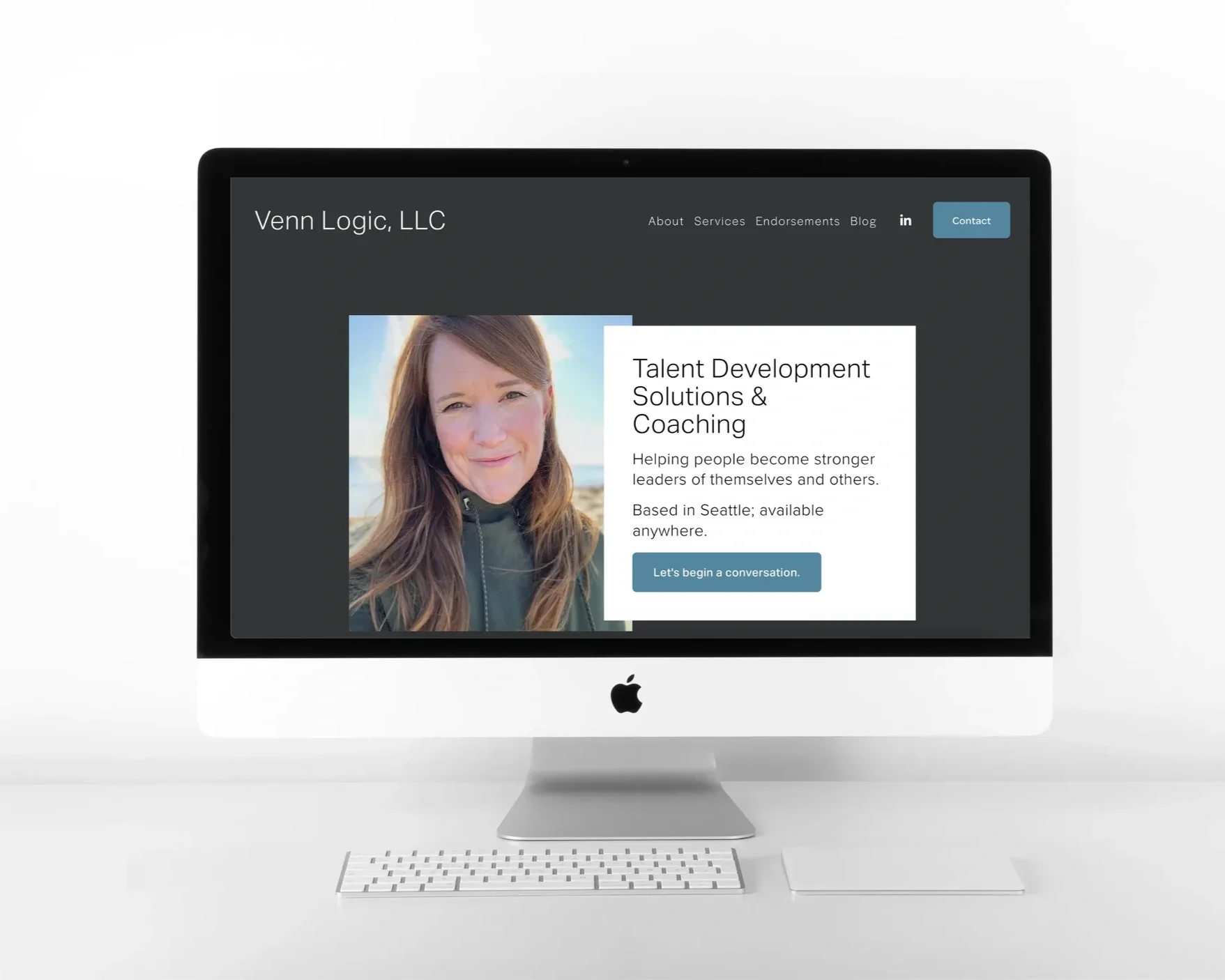 iMac computer screen displaying a website for Venn Logic, LLC, featuring a woman with long brown hair and a dark jacket, alongside text about talent development and coaching, with a blue button labeled 'Let's begin a conversation.'