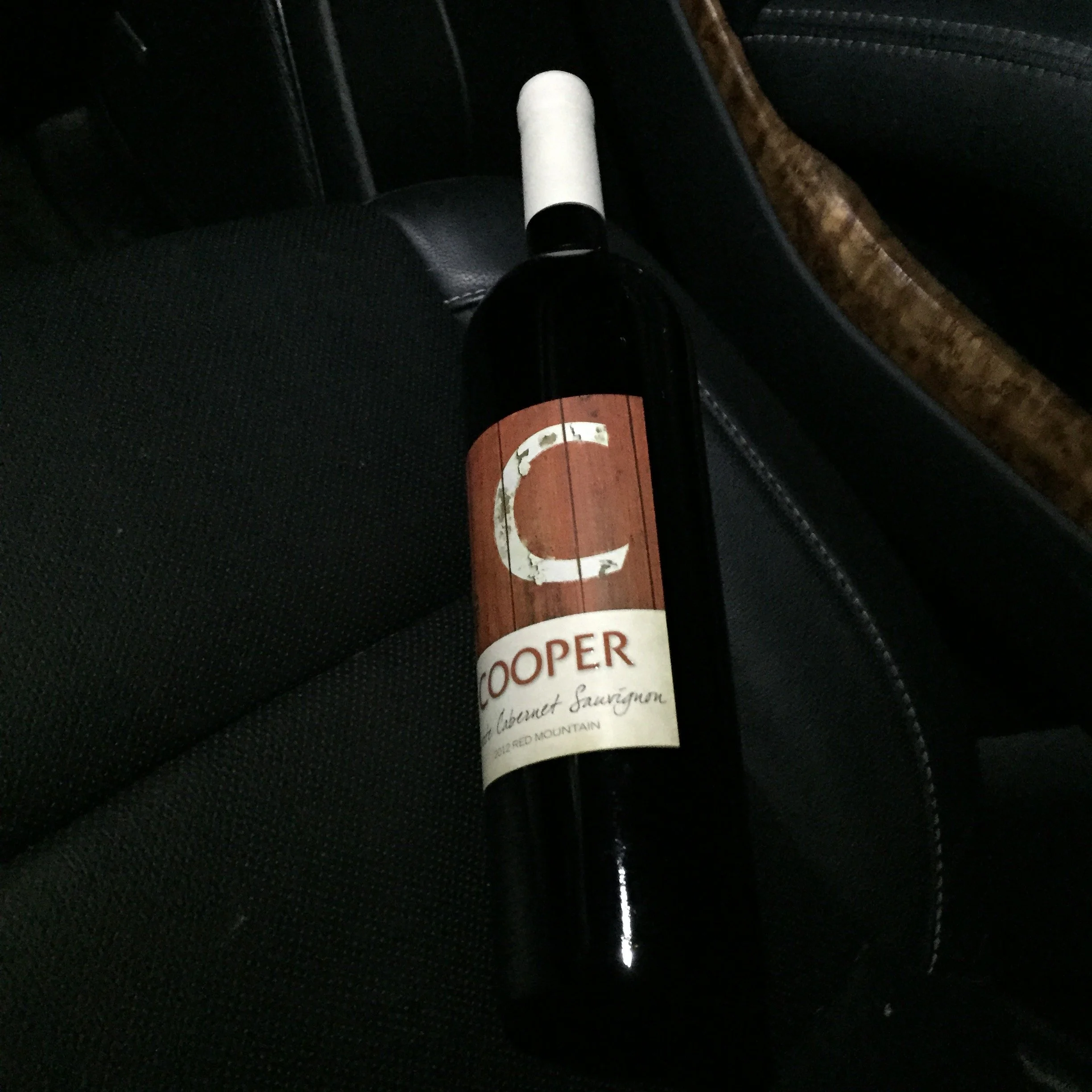 A bottle of Cooper Cabernet Sauvignon wine resting on a black car seat.