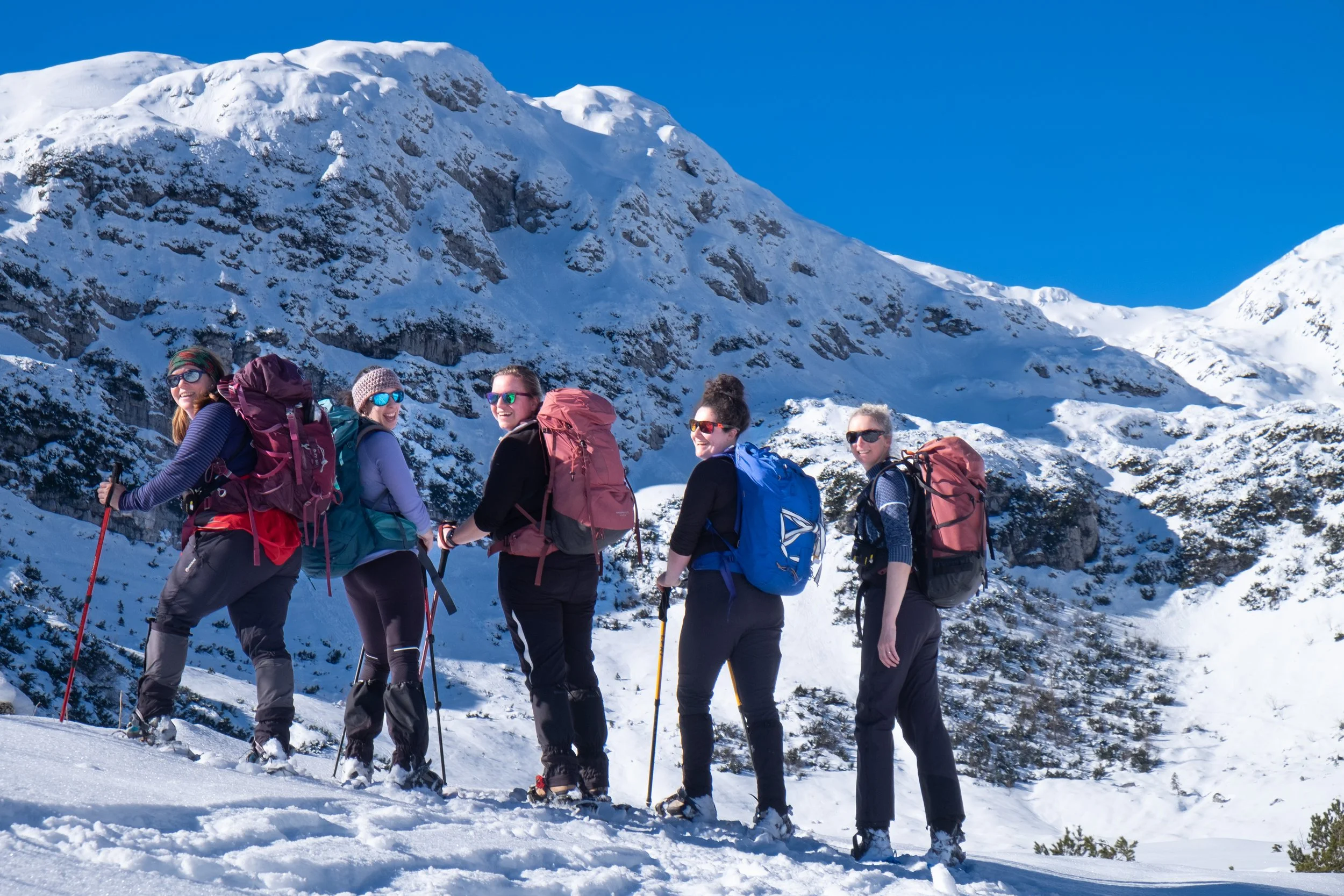 Group of five women hiking in snow-covered mountains with blue sky.