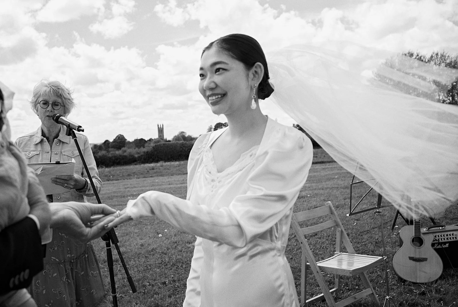 A bride smiles as the groom places a ring on her finger.