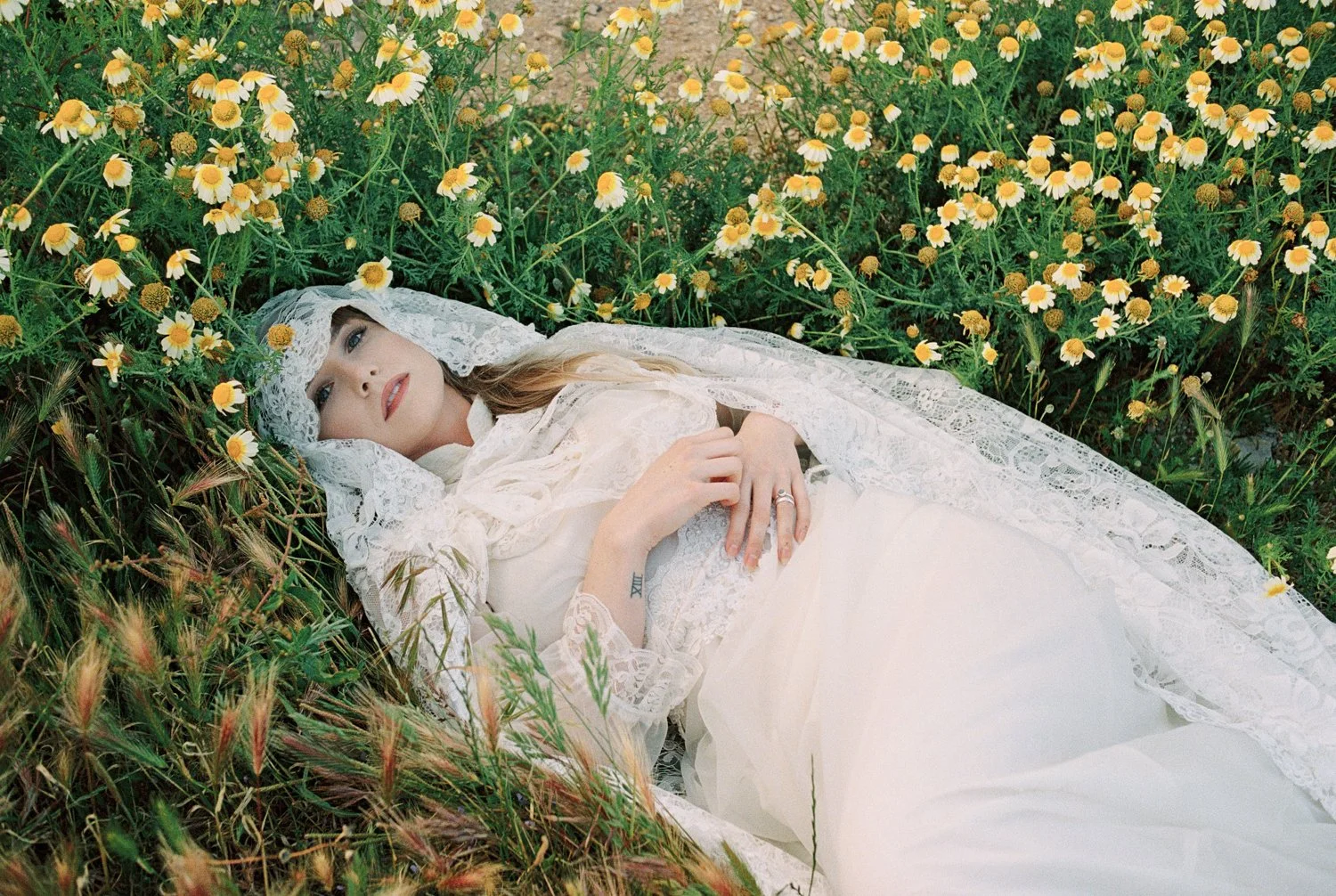 Bride laying on field of flowers on vintage dress in lisbon.
