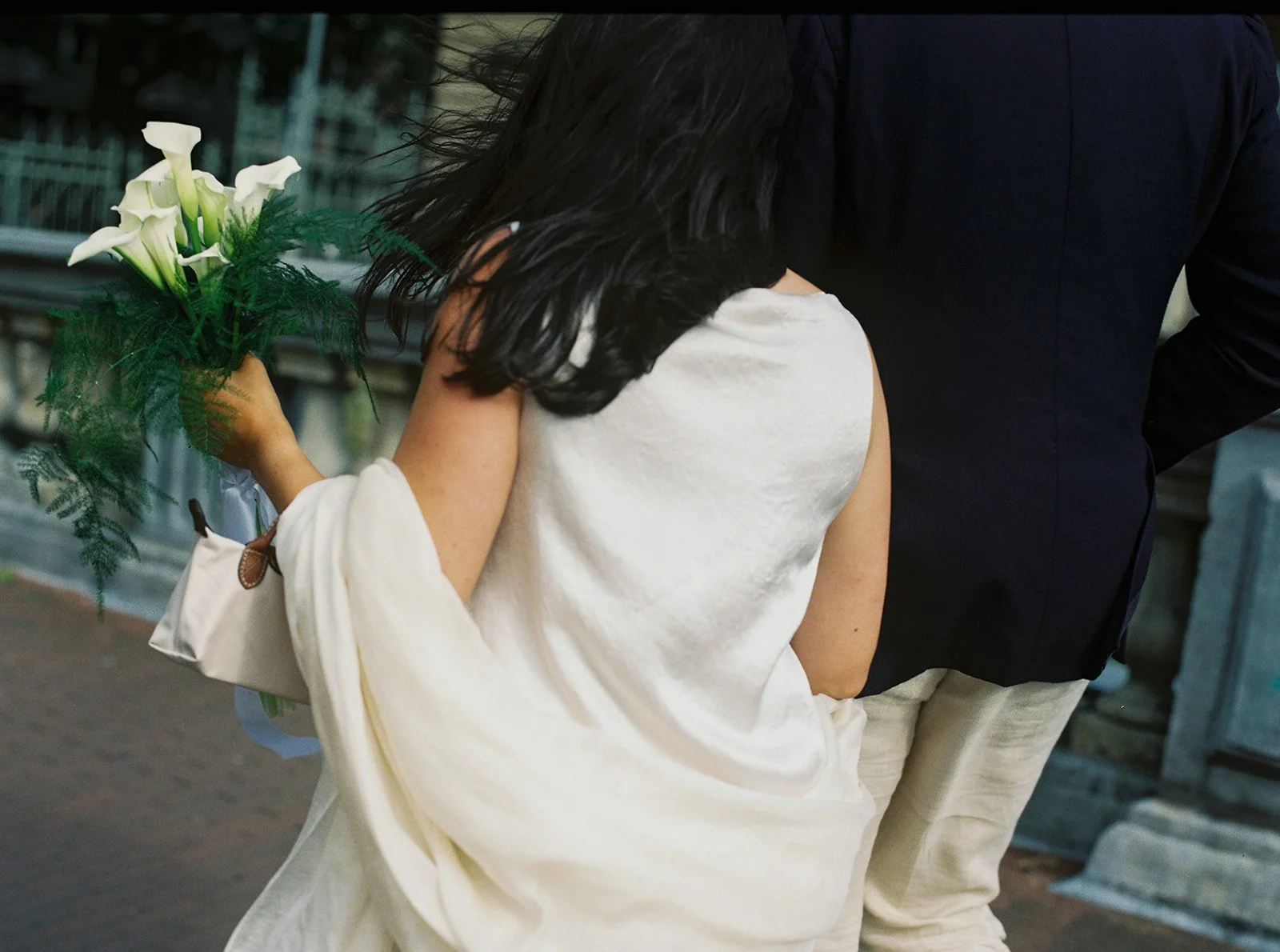 A bride in modern dress holding stylish bouquet walks beside groom captured on film by wedding photographer in Lisbon