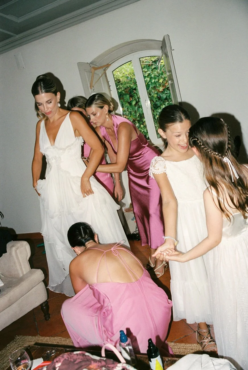 Bridesmaids in pink dresses helping bride getting ready in Algarve before wedding.
