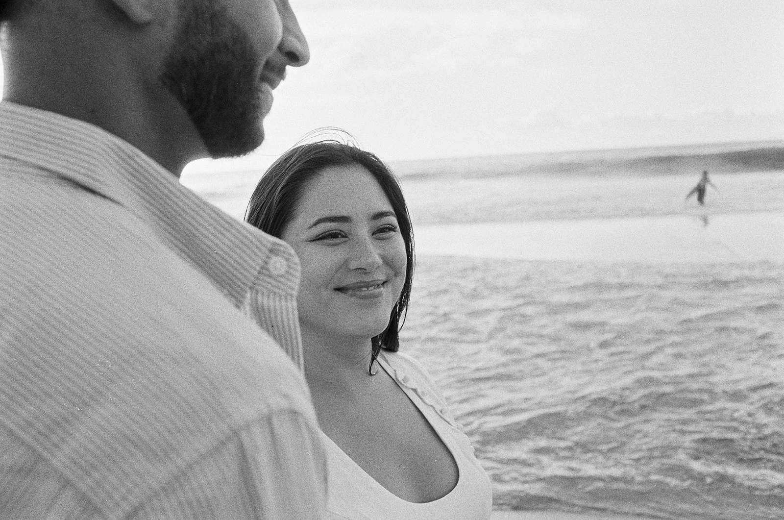 Bride smiling and groomby the beach, with ocean and sky behind them in black and white film.