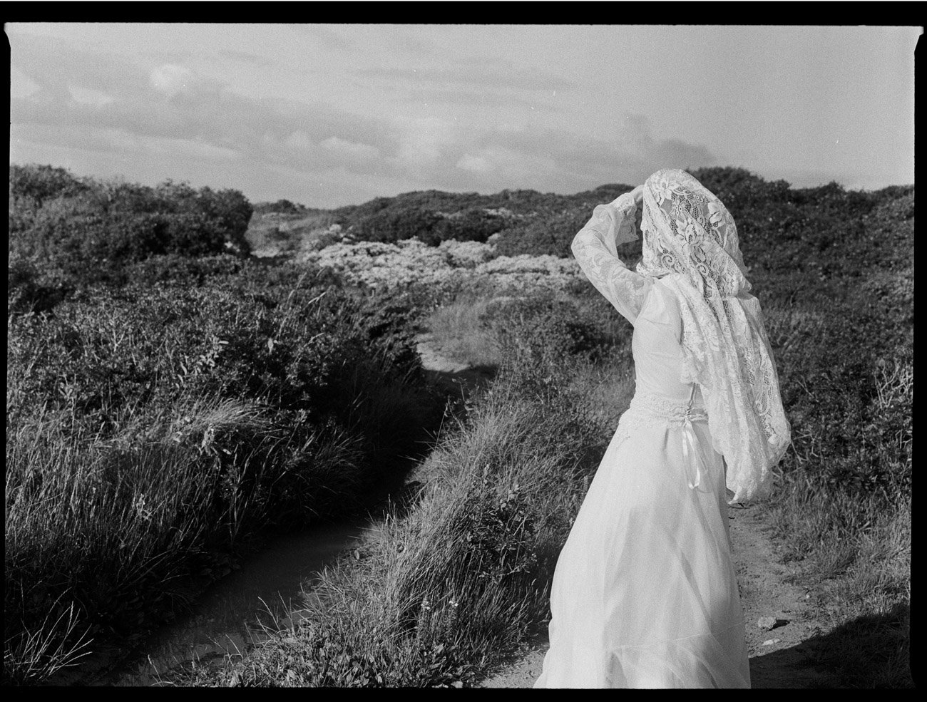 Authentic, cinematic scene of bride walking alone down a wild landscape, captured on BW film by wedding photographer in Lisbon