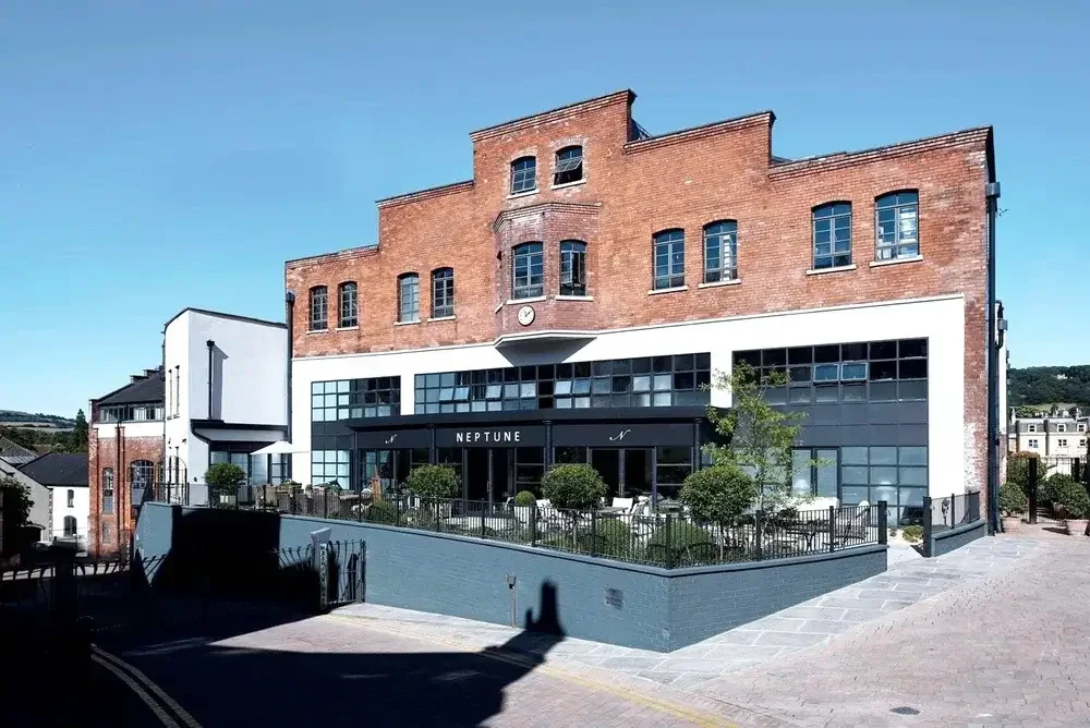 Large-scale historic brick industrial building converted into a modern mixed-use development with commercial frontage and outdoor terrace space.