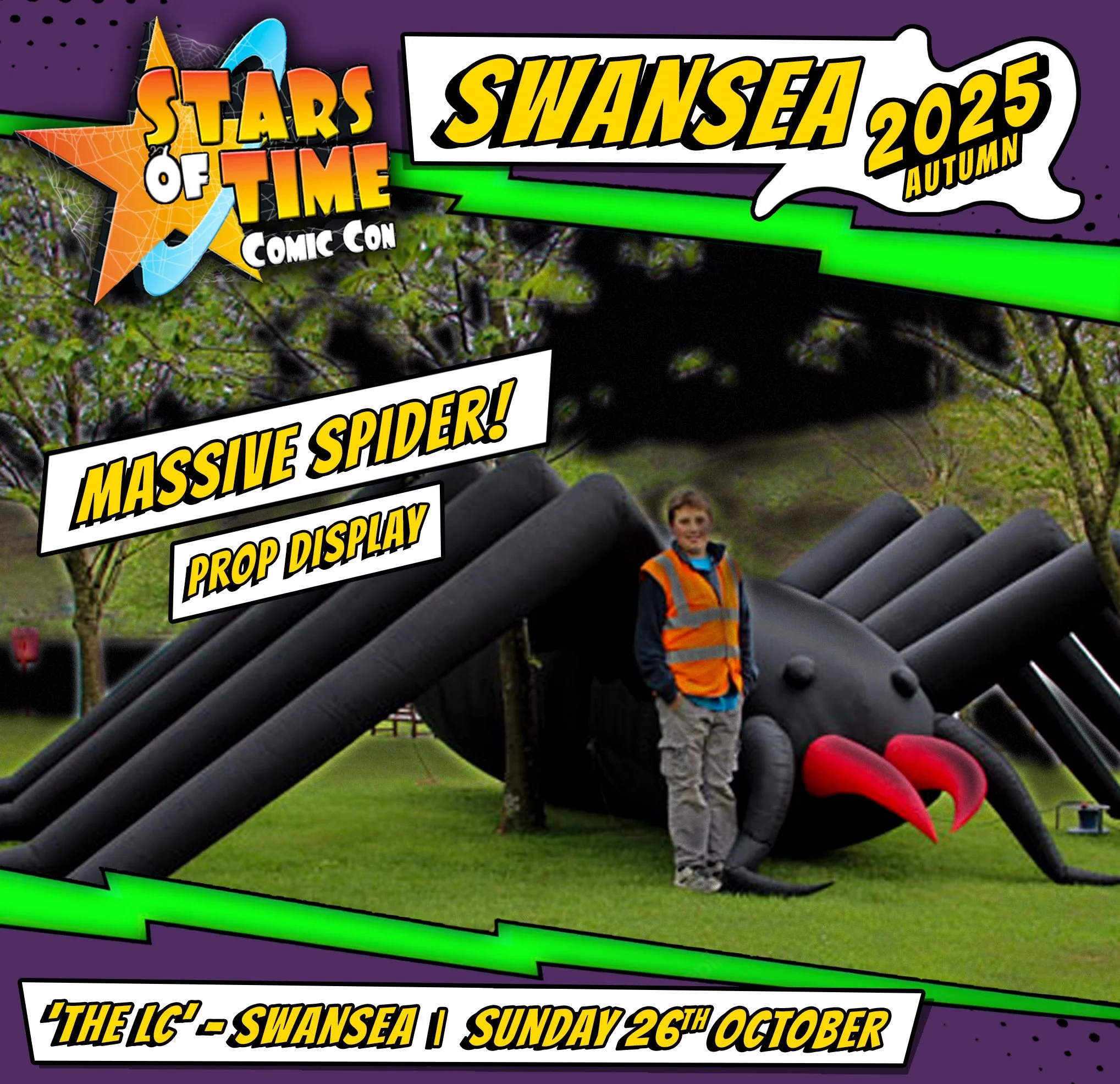 A person standing next to a giant inflatable spider at an event called Stars of Time Comic Con in Swansea, autumn 2025, featuring a large black spider with red fangs and multiple legs, with trees and grass in the background.