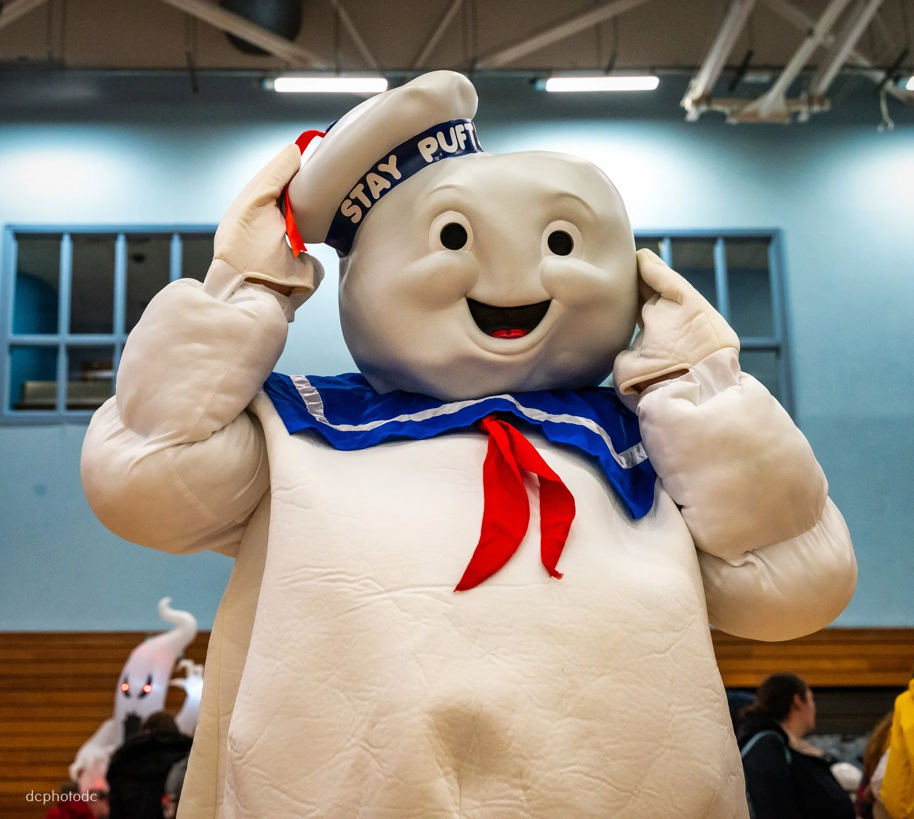 Person dressed in mascot costume resembling a happy steamed bun character, wearing a sailor outfit with blue collar and red necktie, and a white cap labeled "Stay Puff".