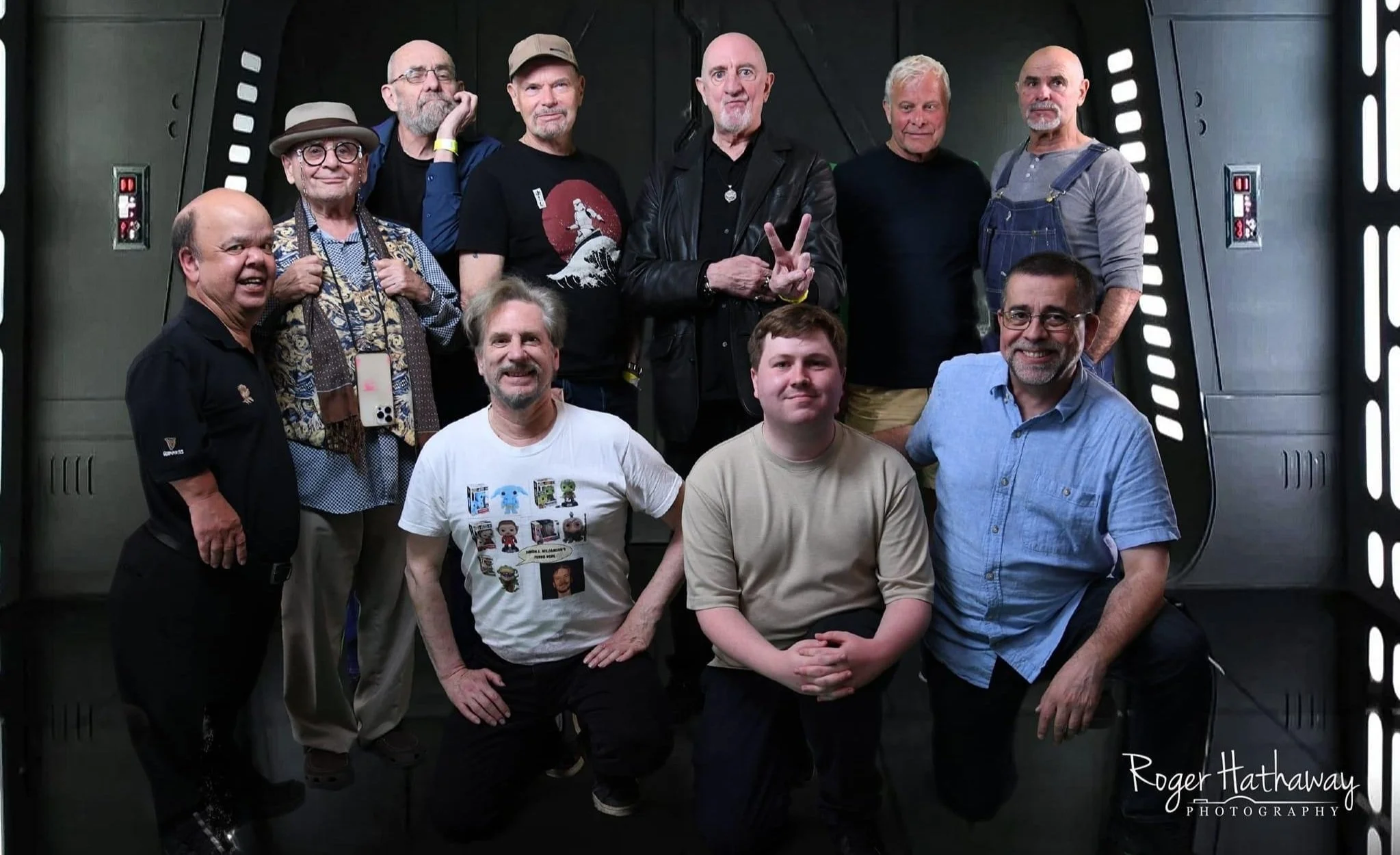 Group of Star Wars Actors and their agent posing together in a sci-fi themed room. Background resembles a spaceship interior, with dark walls and illuminated panels.
