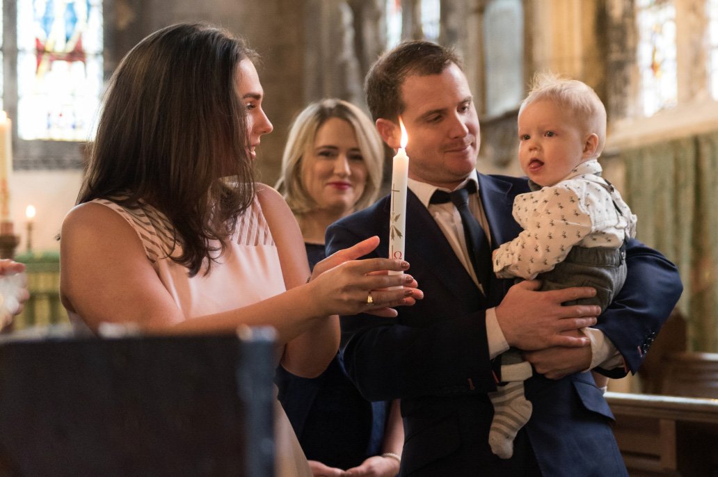 parents hold child and candle at church Christening