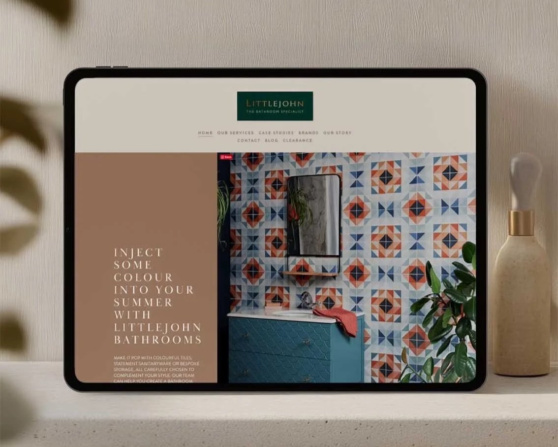 Tablet displaying a webpage for Littlejohn Bathrooms with a colorful tile background, a mirror, a sink, and a plant, on a bathroom countertop.