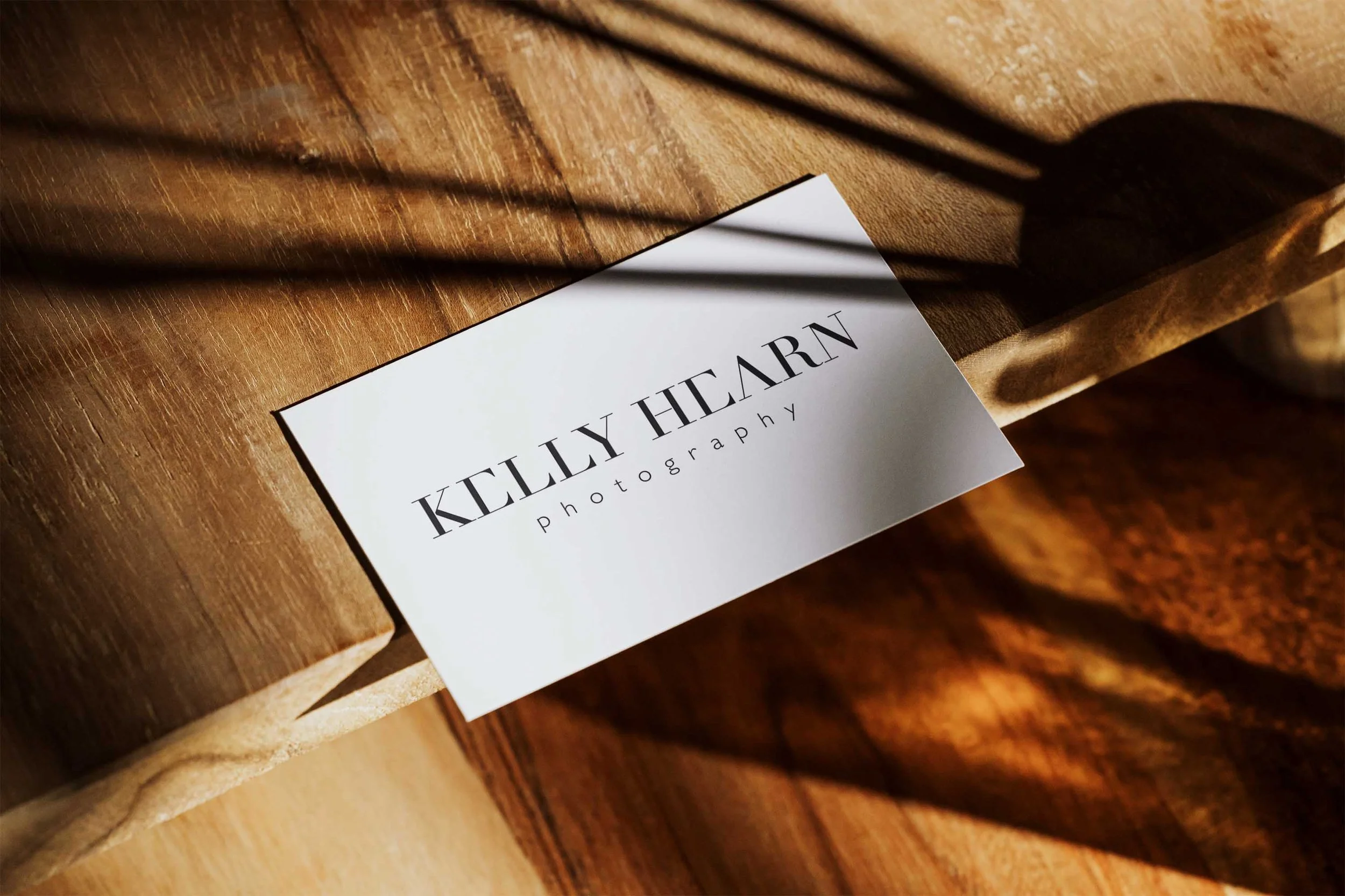 A business card for Kelly Hearn Photography placed on a wooden surface, with shadows cast over it.