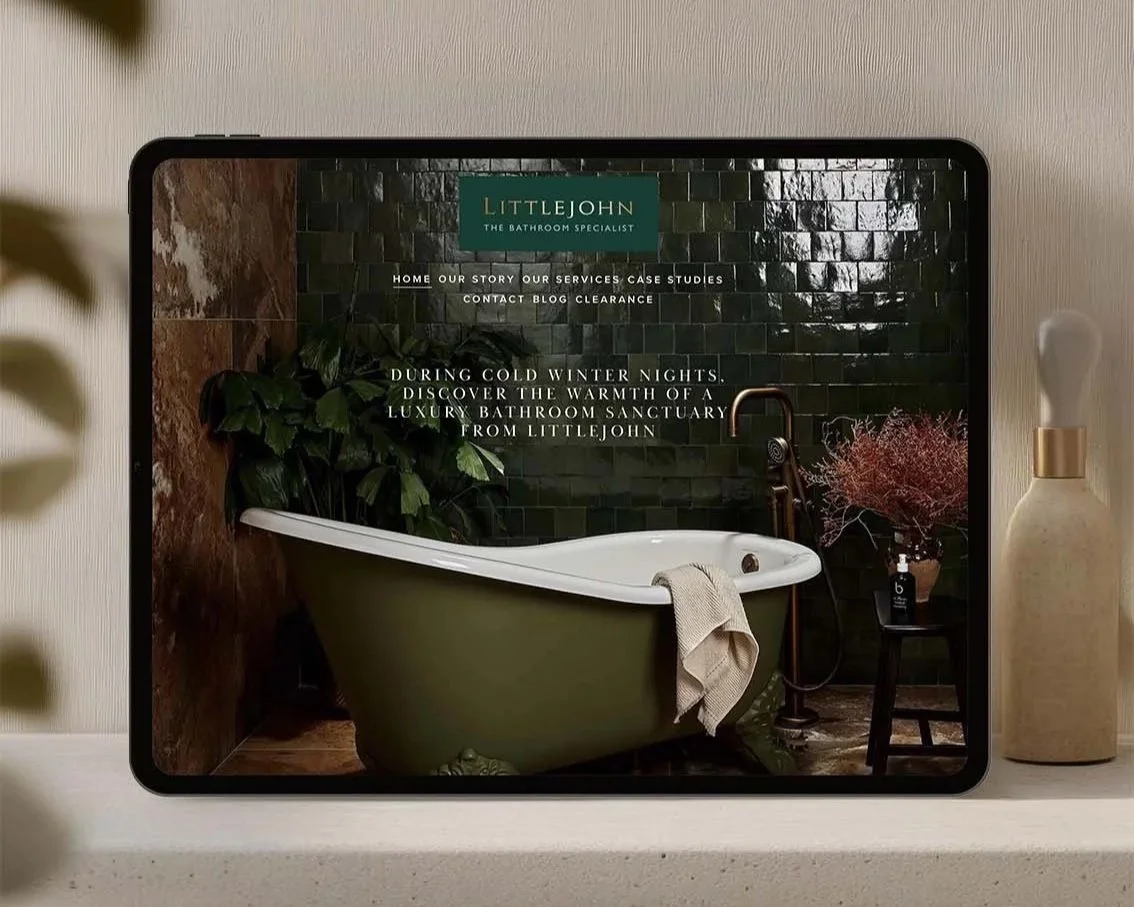 A tablet displaying a website for Littlejohn, a bathroom specialist, with an image of a luxurious bathroom bathtub surrounded by green plants and decor.