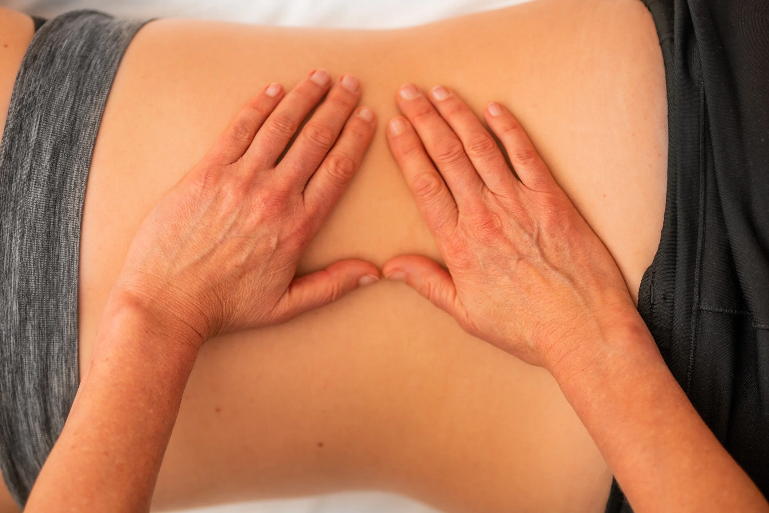Hands giving a massage on a person's lower back with gray and black clothing visible.