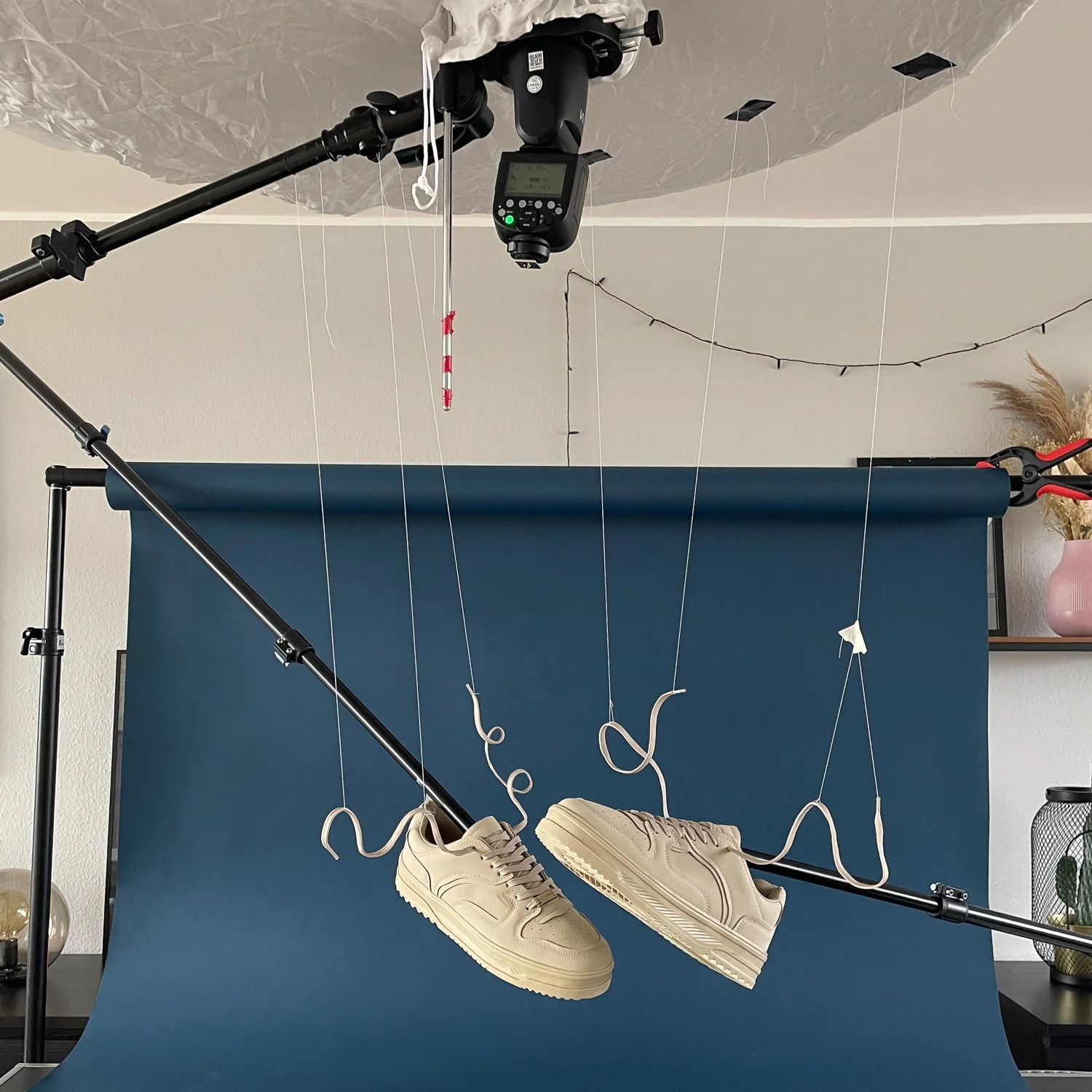 Aufnahmen von einem Fotostudio, in dem weiße Turnschuhe an Drähten hängen vor einem blauen Hintergrund.