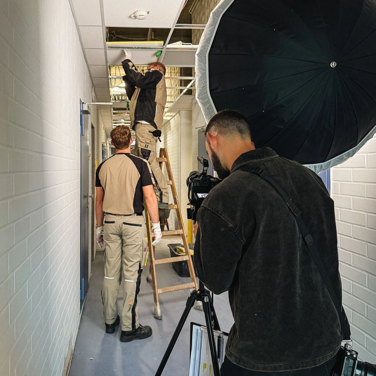 Fotografen nimmt ein Bild von drei Bauarbeitern auf, die in einem Flur an einem Gerüst arbeiten und eine Leiter benutzen.