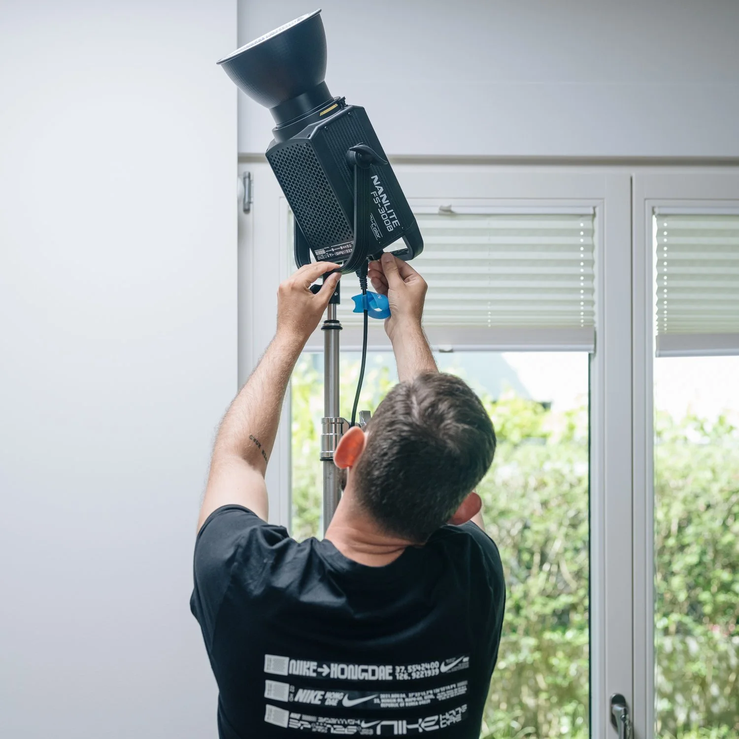 Ein Mann richtet eine Studioleuchte in einem Raum mit großen Fenstern aus.