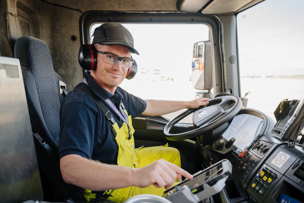 Lkw-Fahrer im Fahrerhaus, trägt Schutzhelm und Kopfhörer, bedient das Navigationsgerät, sitzt am Steuer eines Lastwagens, mit Blick auf die Straße draußen