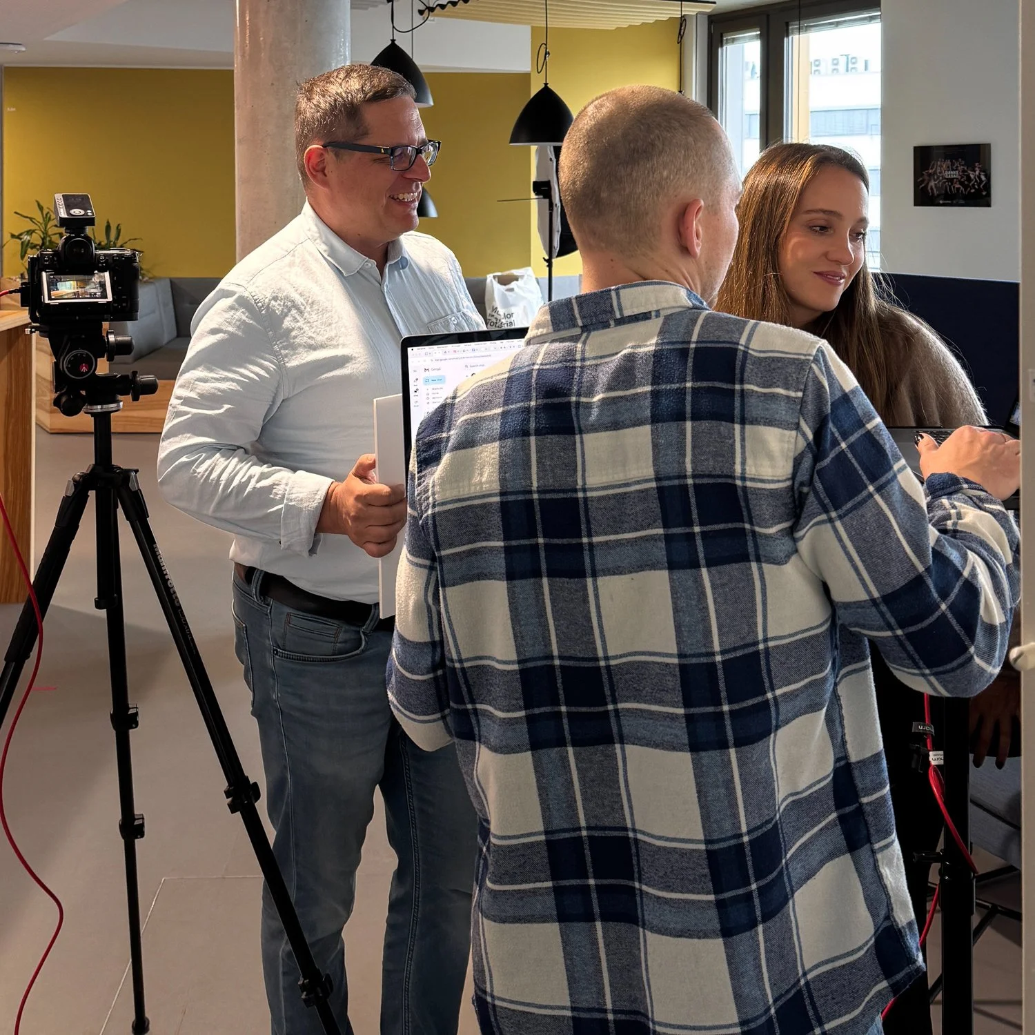 Drei Menschen stehen in einem Raum mit Kamera und Laptop, sie sprechen und lachen miteinander.