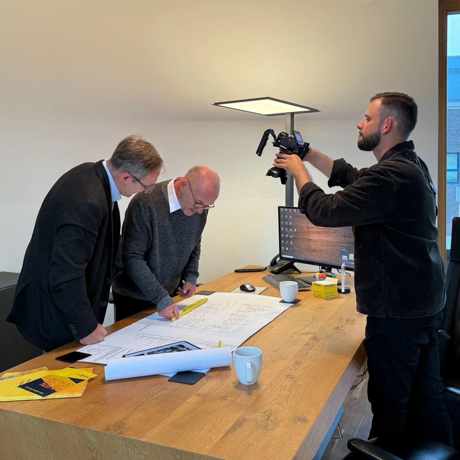 Zwei Männer mit Messwerkzeugen und eine Kameraaufnahme eines Mannes im Büro, vor einem Computer, mit Projektplänen auf dem Tisch.