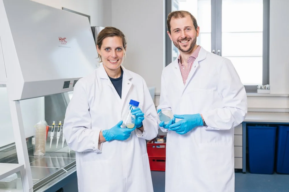 Zwei Wissenschaftler in weißen Kitteln mit blauen Handschuhen in einem Labor, die Proben halten.