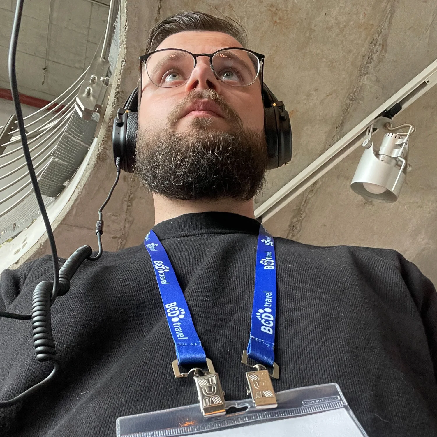 Ein Mann mit Brille und Bart trägt Kopfhörer und einen lila Ausweis mit dem Schriftzug 'BÖD Travel'.