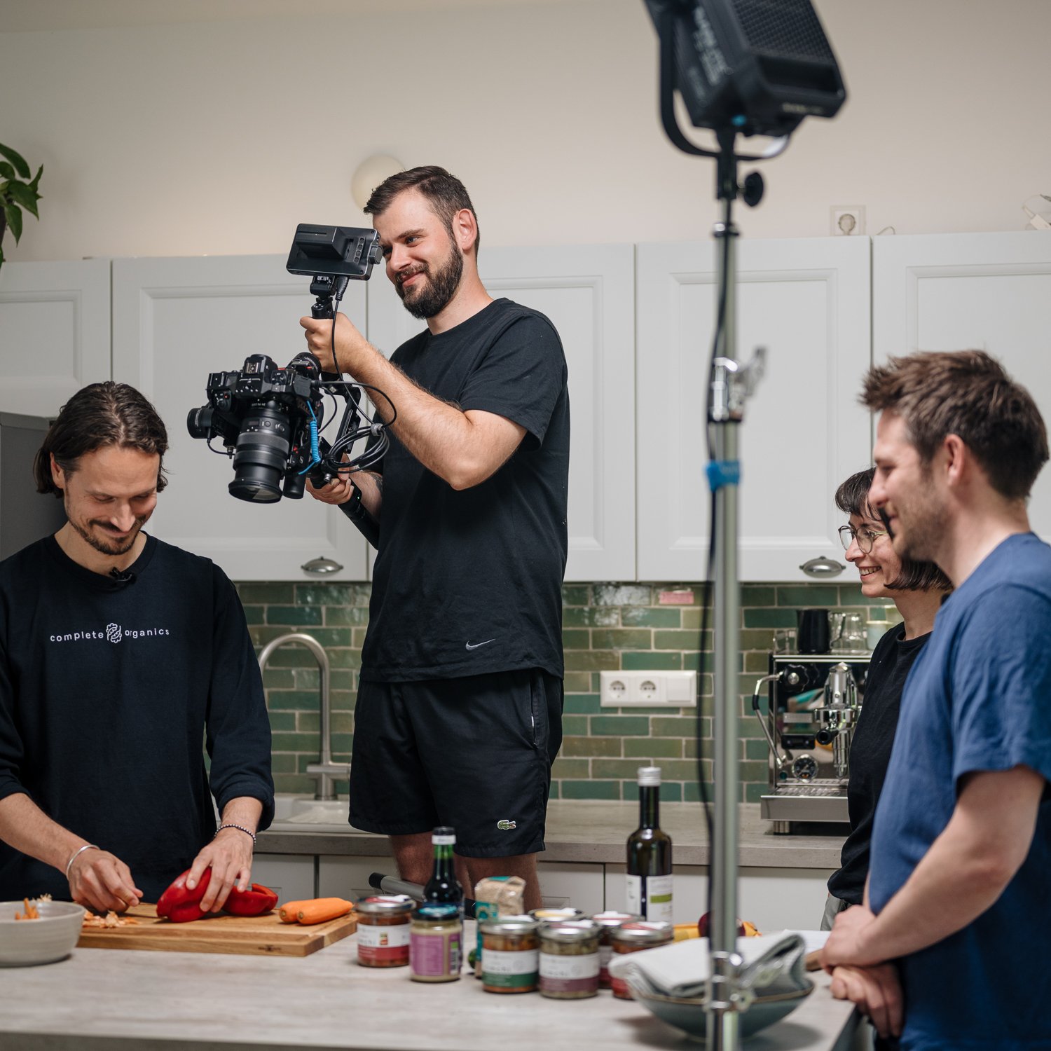 Filmdreh in einer modernen Küche, mehrere Personen, einer filmt, andere bereiten Lebensmittel vor.