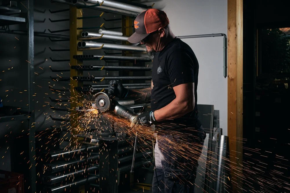 Mann beim Schleifen eines Metallstabs in einer Werkstatt, mit Funkenflug umgeben.
