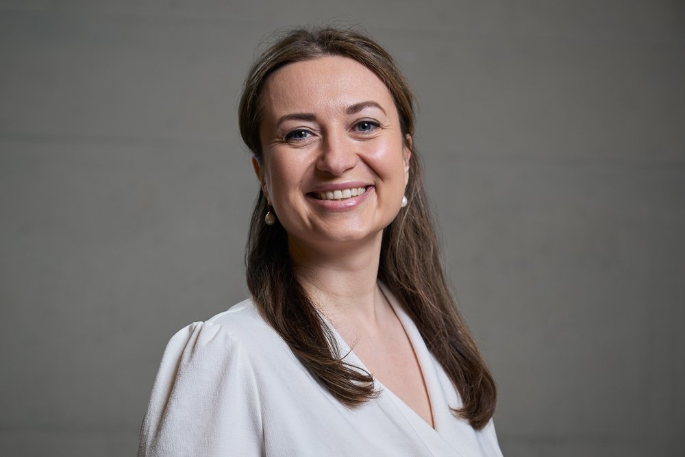 Ein lächelndes Mädchen mit braunen Haaren vor einem grauen Hintergrund.