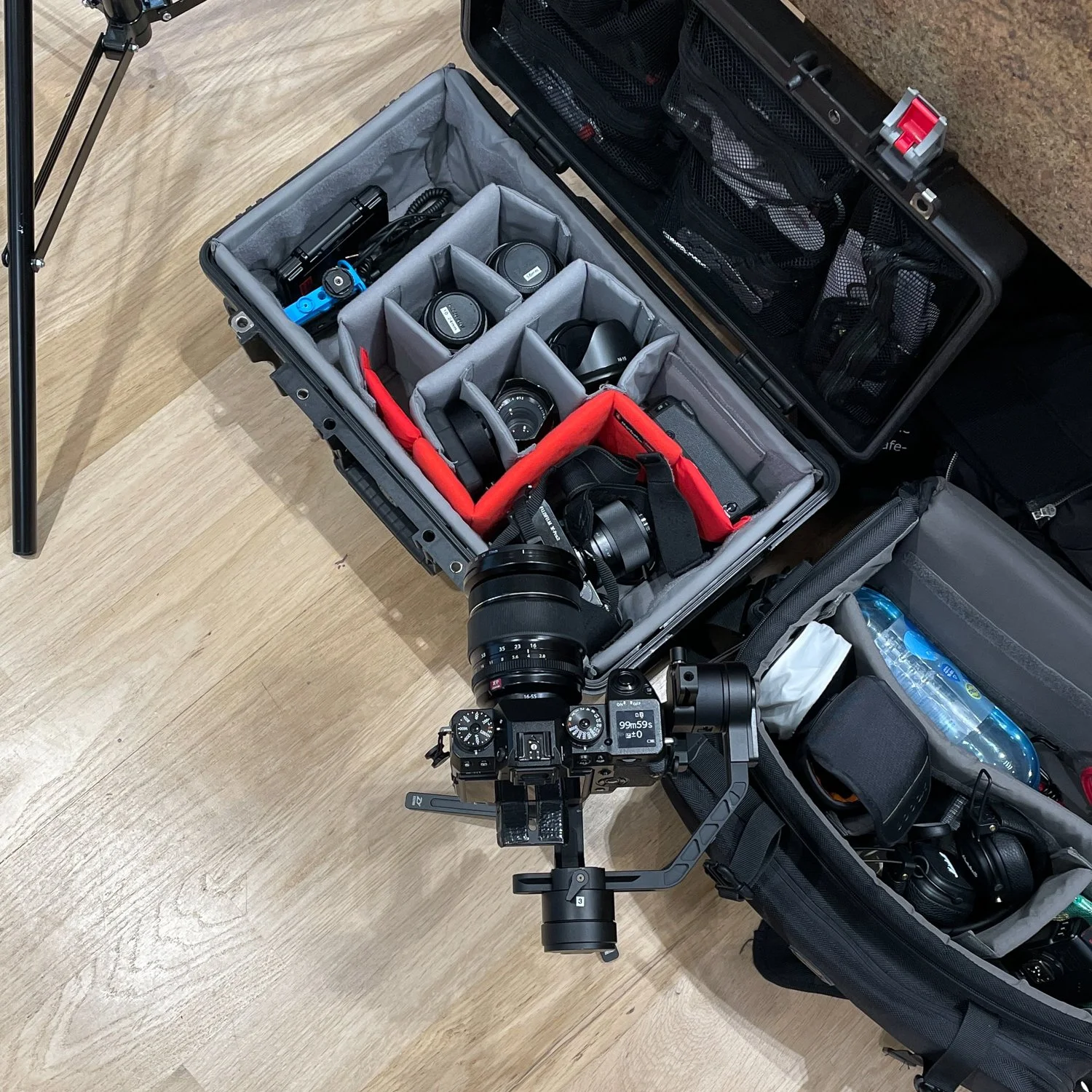 Fotografie einer Kameraausrüstung mit Zubehör, geordnet in einer gepolsterten Kameratasche, inklusive Kamera, Objektiven, Wasserflasche und weiteren Zubehörteilen.