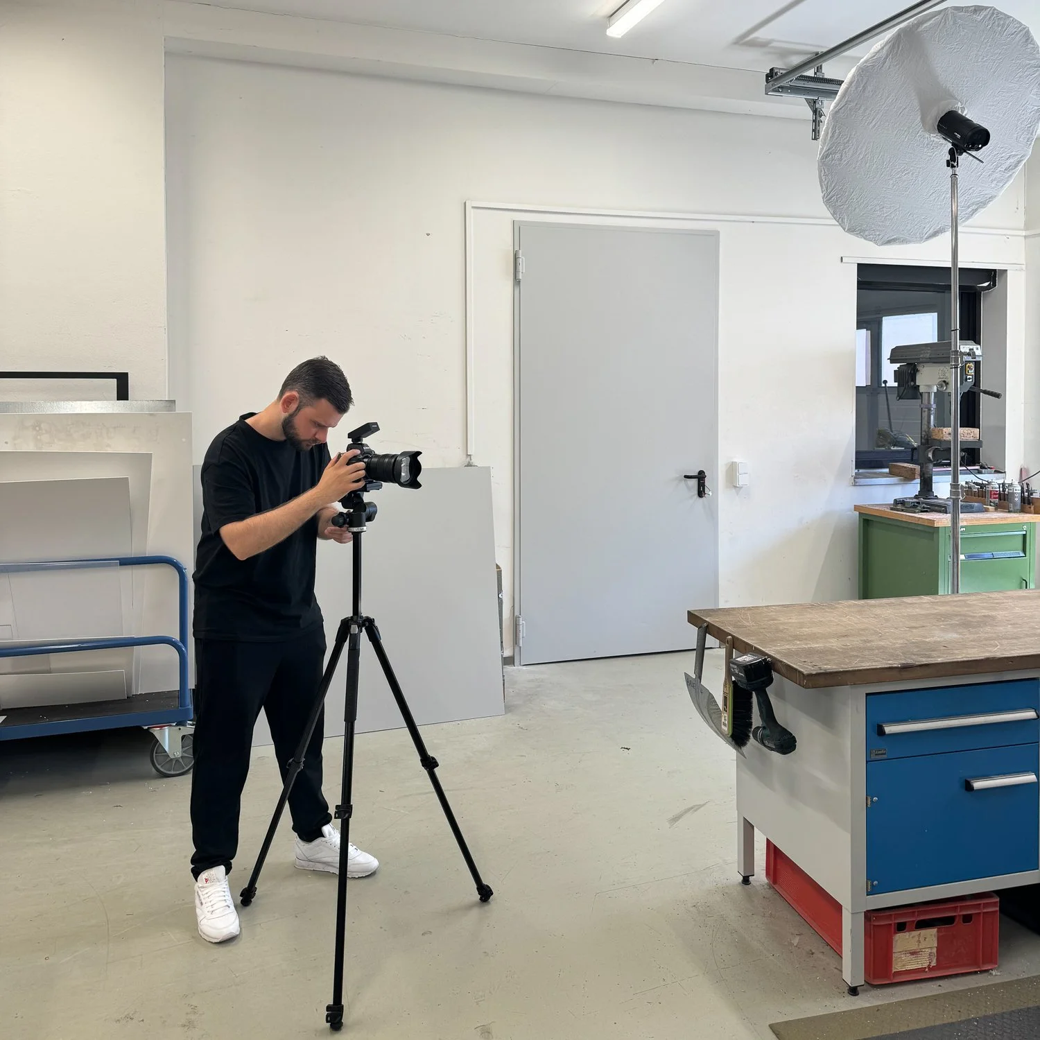 Ein junger Mann fotografiert in einem Fotostudio mit professionellem Licht. Das Studio ist schlicht mit Werkbank und Werkzeugen im Hintergrund.