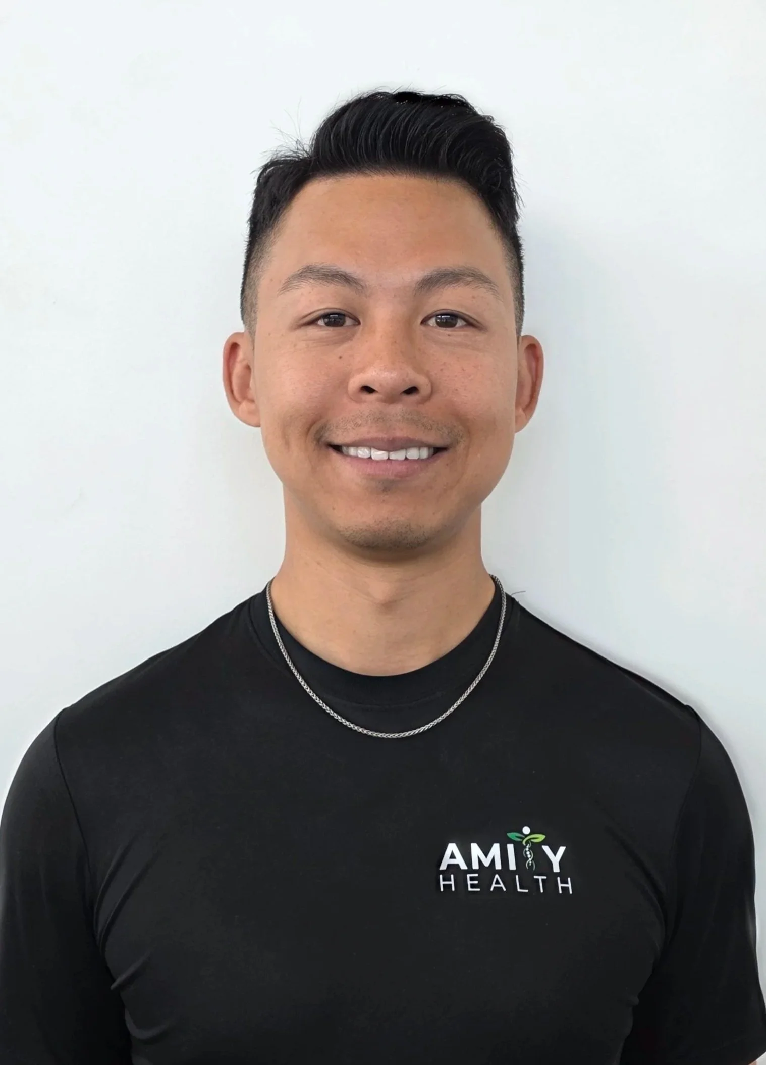 Dr. Paul Seto Scarborough Chiropractor man with short black hair, wearing a black T-shirt with 'AMIY HEALTH' logo, standing against a plain white background.