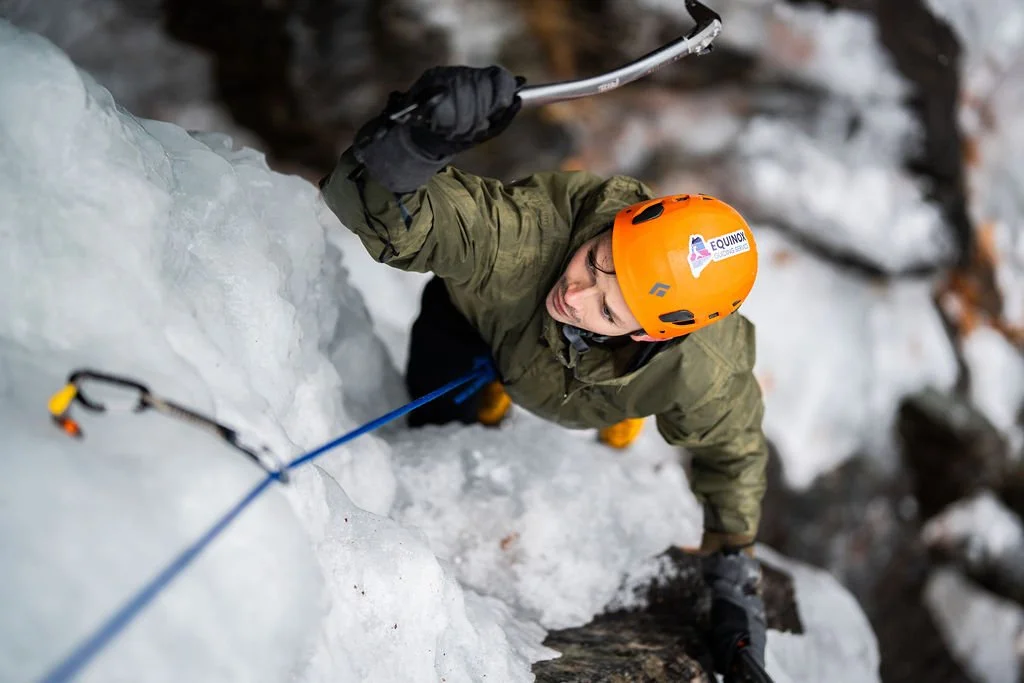 Person climbing an ice wall with safety gear and helmet during ice climbing adventure.