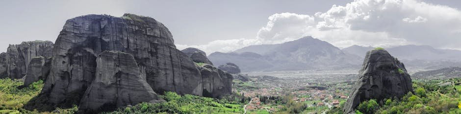Large rocky formations in a green landscape with a mountain range and cloudy sky in the background.