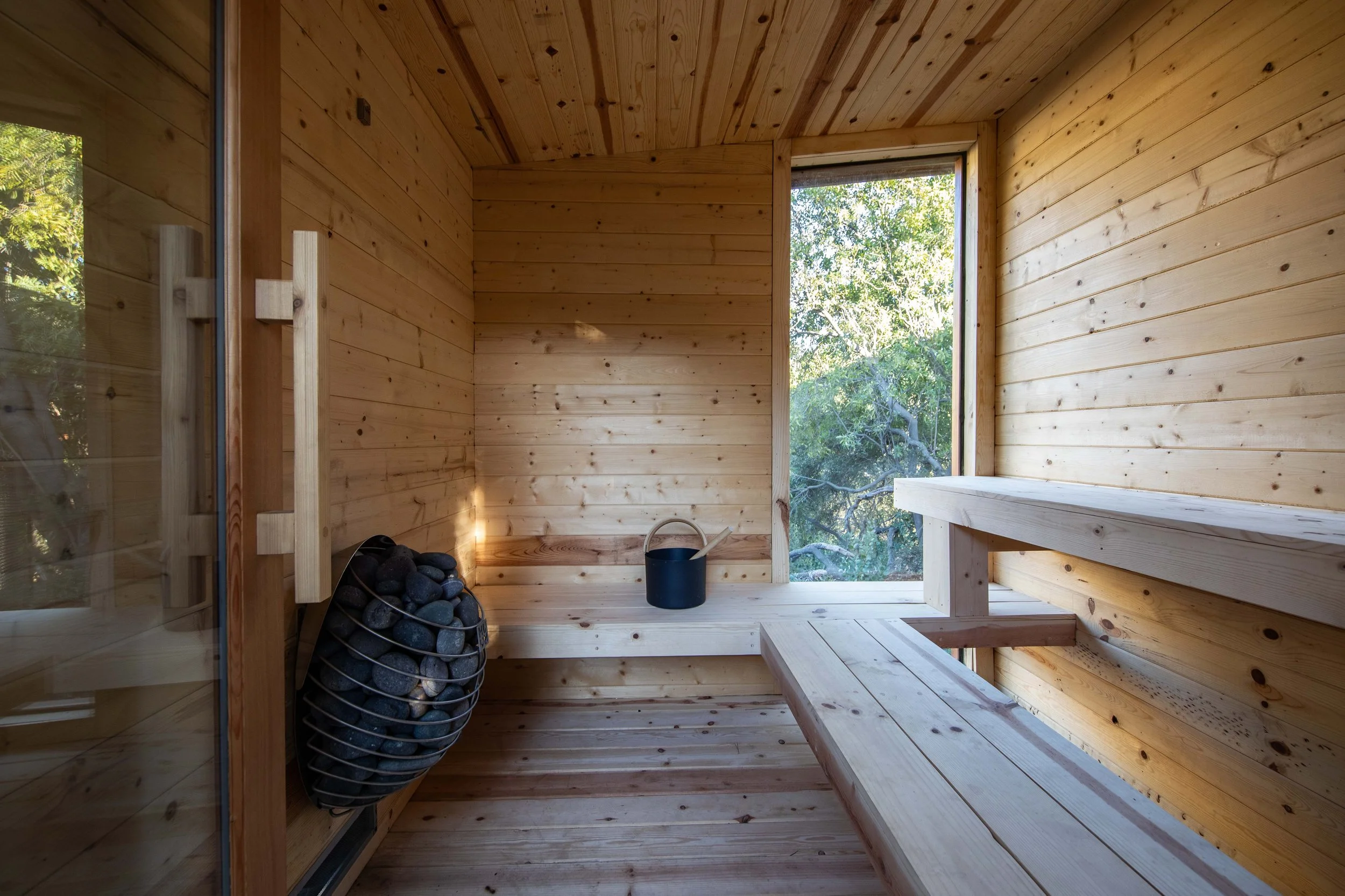 Sauna interior with cedar bench and picture window, native planting view, residential wellness landscape