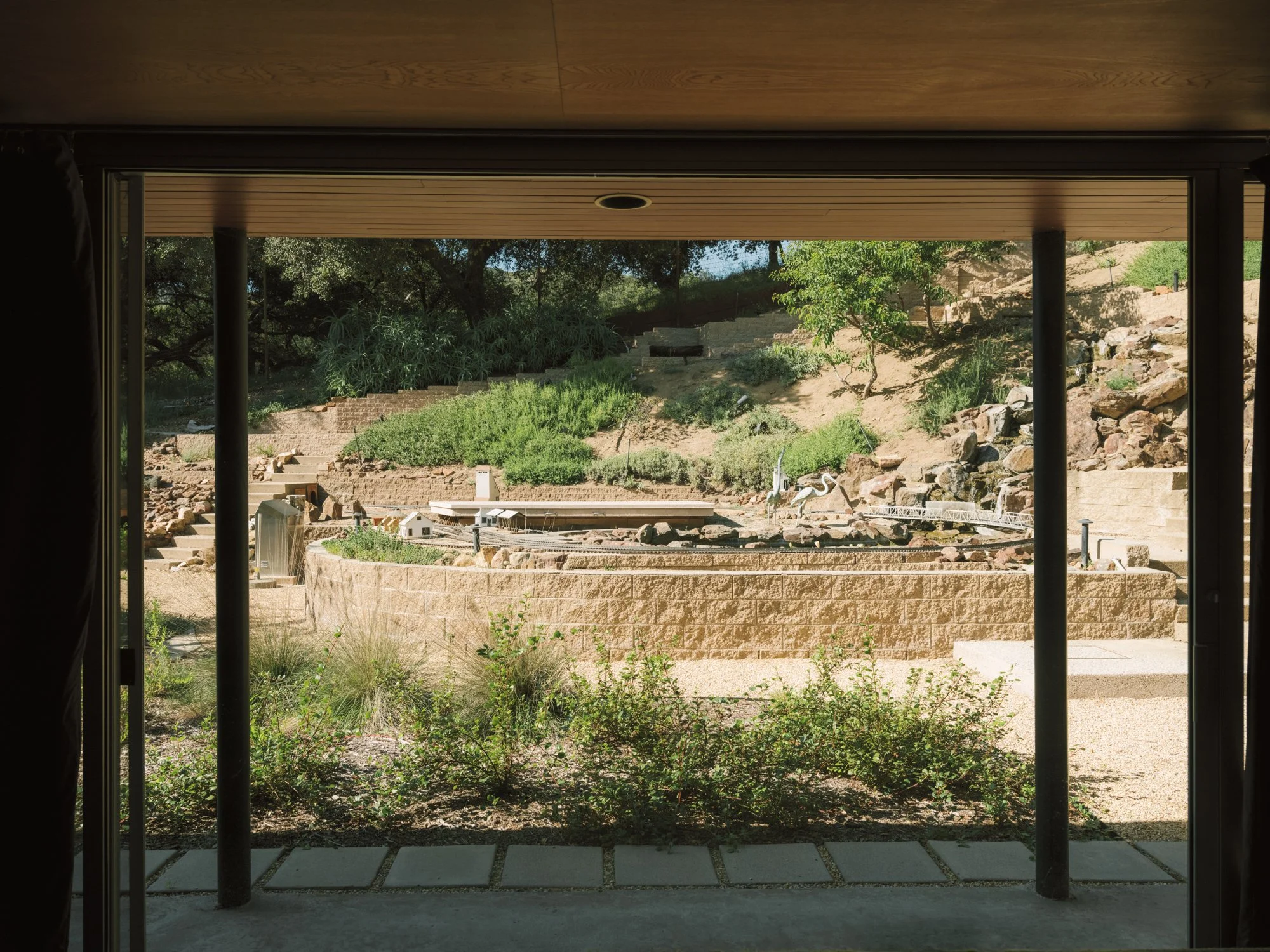 View through steel-frame floor-to-ceiling glass doors from a Raphael Soriano residence overlooking a terraced native plant garden in Los Feliz