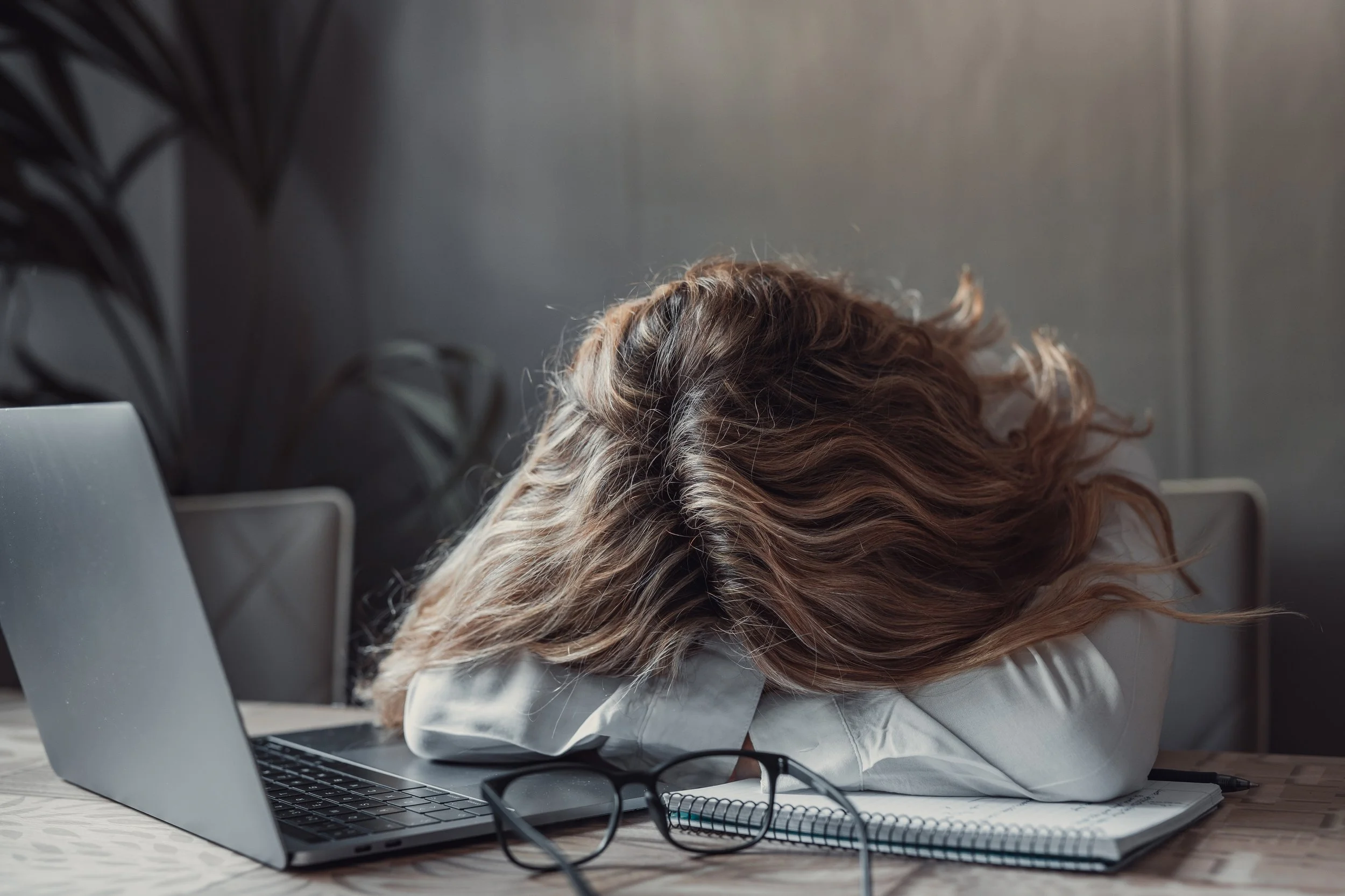 Woman resting her head on her desk from exhaustion and burnout at work.