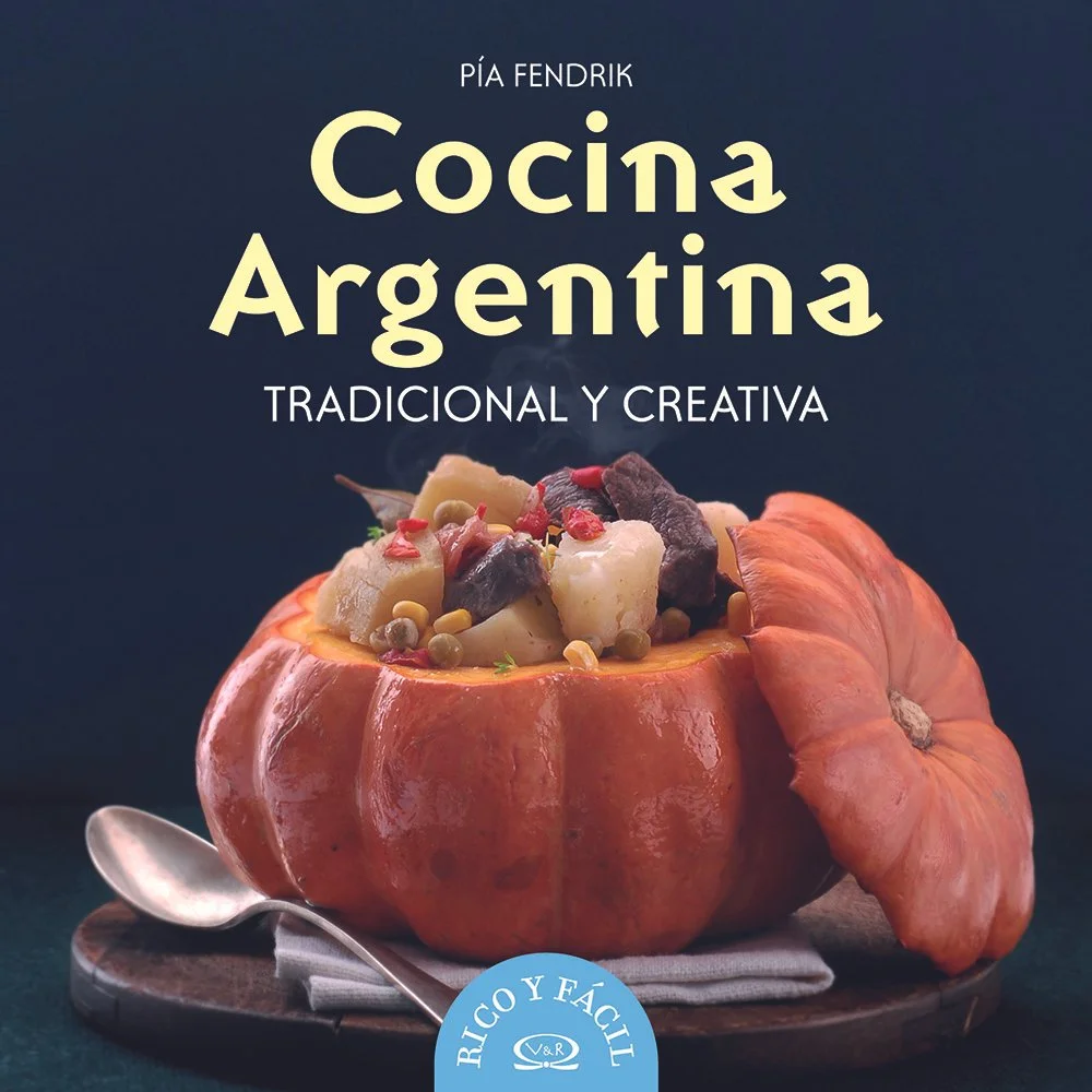 Libro titulado 'Cocina Argentina' de Pía Fendrik, con una calabaza rellena de ingredientes tradicionales sobre una mesa con cuchara y plato.