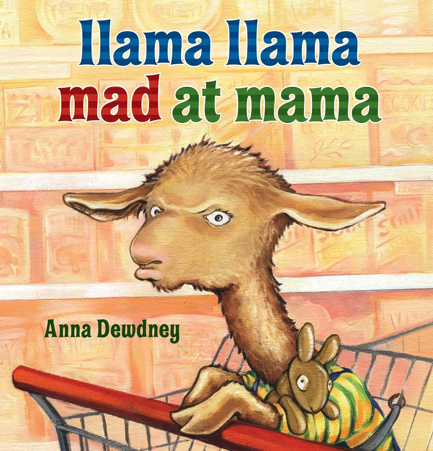 Portada de un libro infantil titulado 'Llama llama mad at mama', ilustración de una llama con expresión molesta en un carrito de compras, sosteniendo un conejo de peluche, con fondo de paredes de ladrillos y estantes.