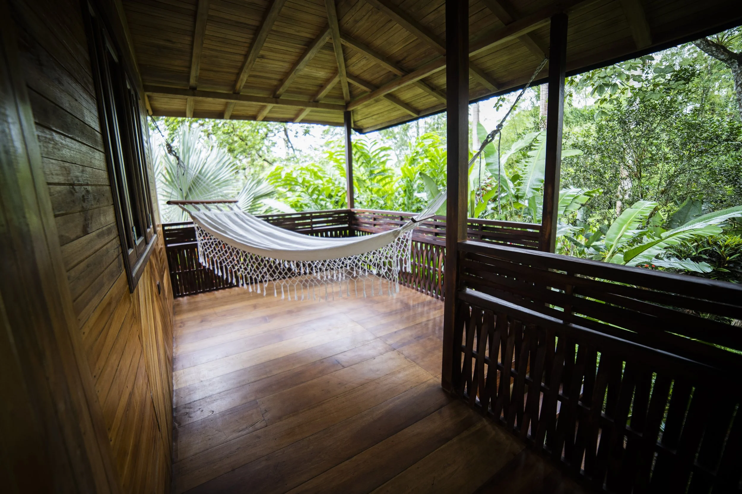Terraza de madera con hamaca en un entorno de vegetación verde.