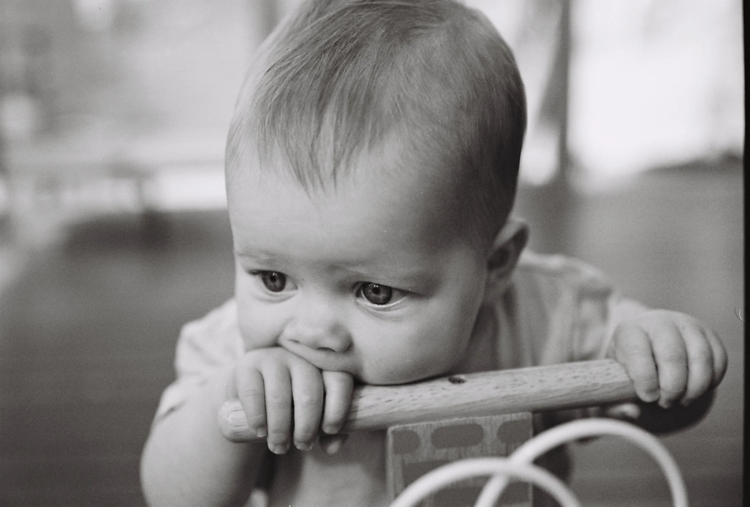 A young child with short hair leaning on a toy with rings, looking to the side with a serious expression.