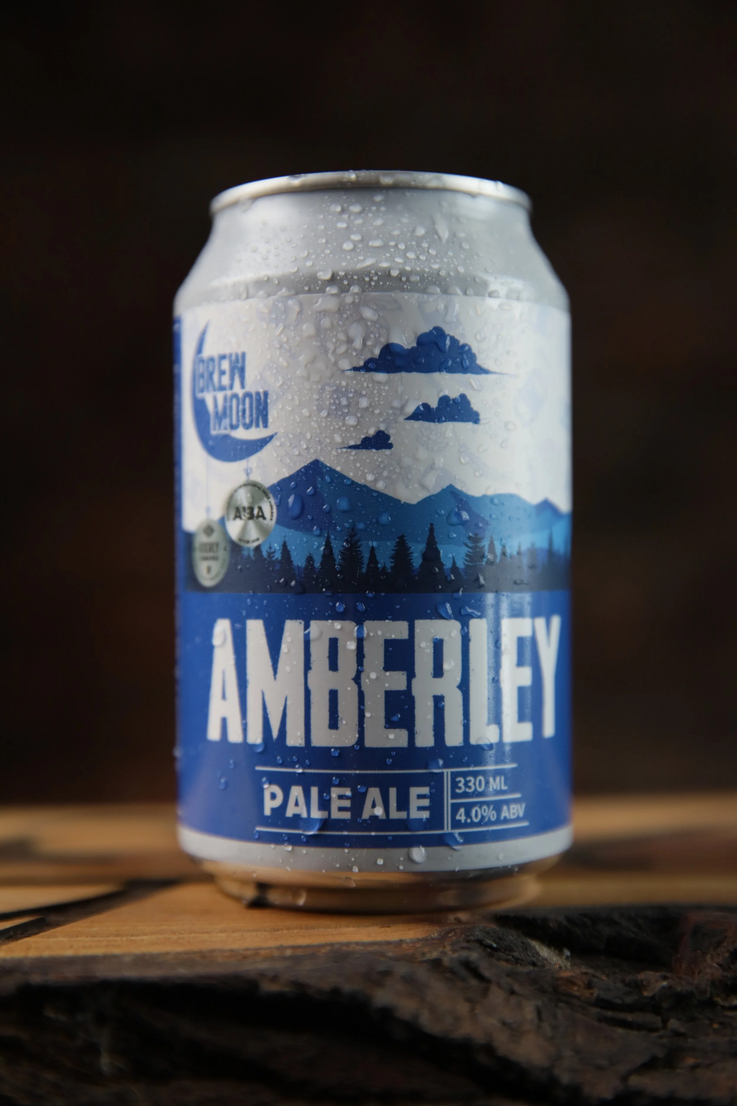 A can of Amberley Pale Ale with water droplets on it, sitting on a wooden surface with a dark background.