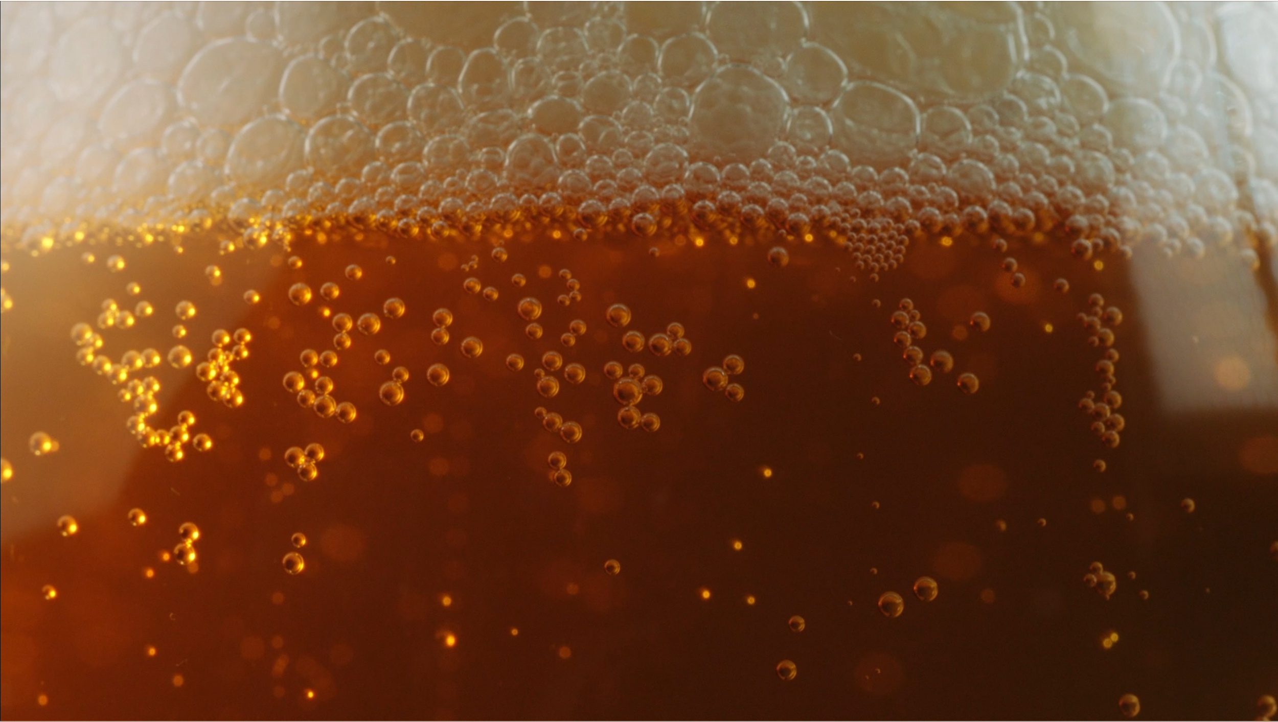 Close-up of effervescent bubbles forming in a glass of dark soda.