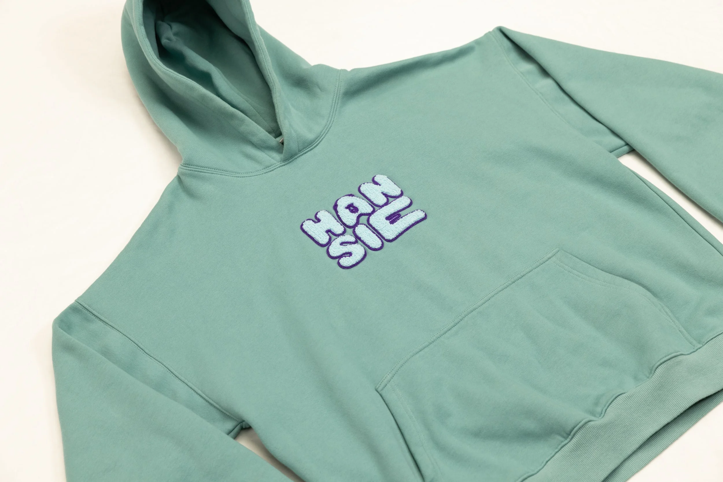 A mint green hoodie with the words 'MAGIC SICK' embroidered on the chest in purple and white.