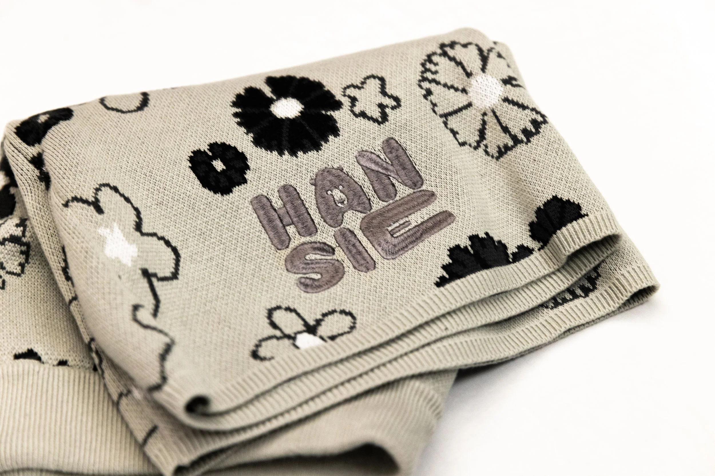 A beige fabric item with black and white floral patterns and the words "HAVE SIE" embroidered in the center.