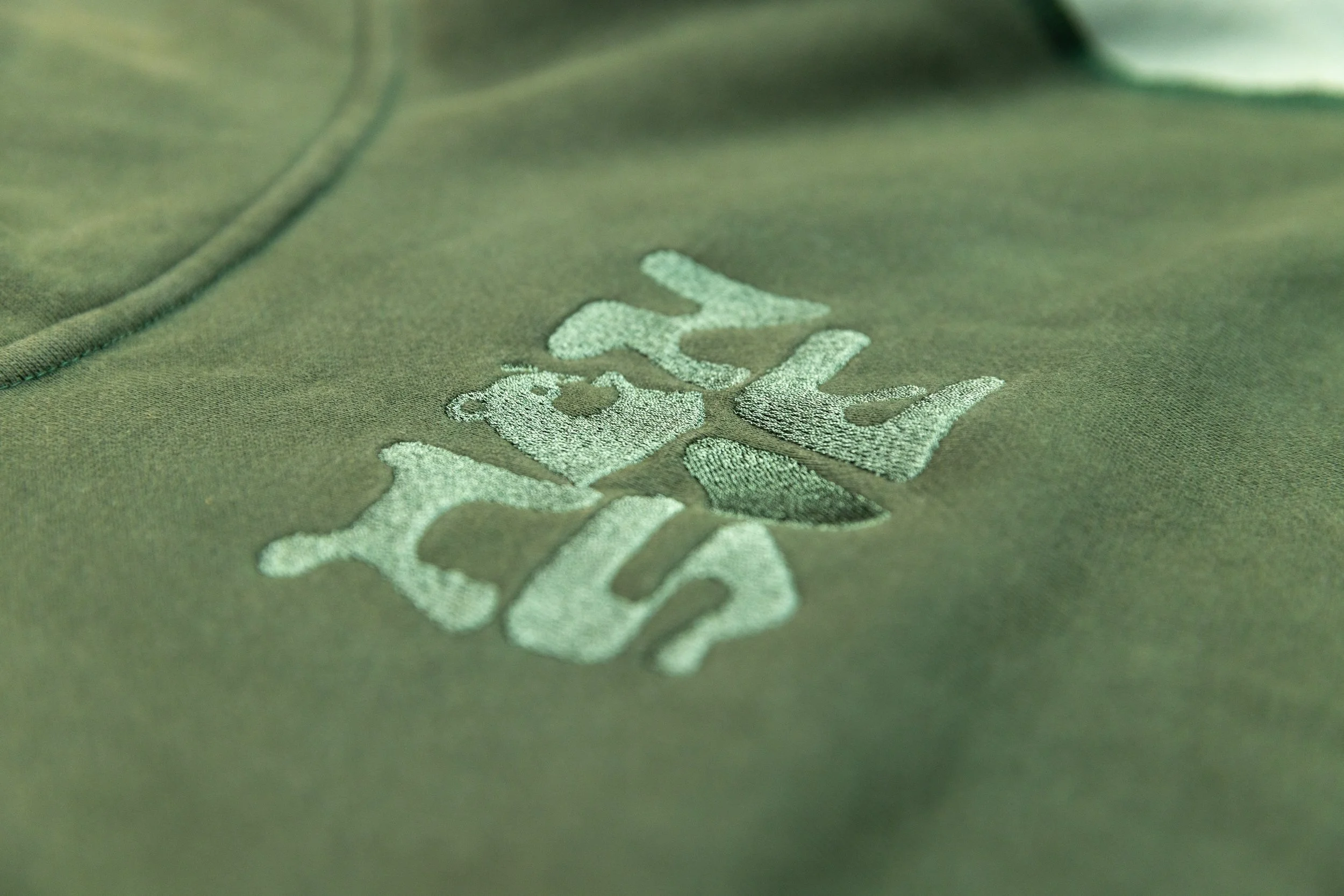 Close-up of green fabric with the word "polo" embroidered in light green thread and a small bear graphic.