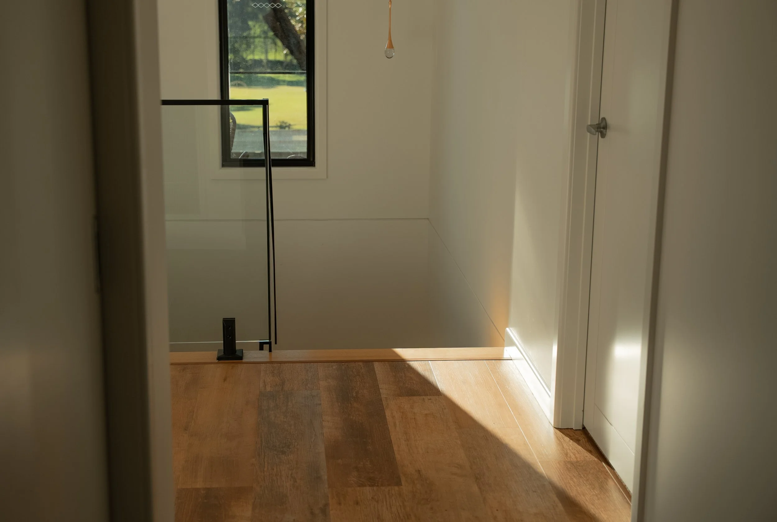 Interior of a house stairway with a window, a hanging pull cord, wood flooring, and a black handrail.