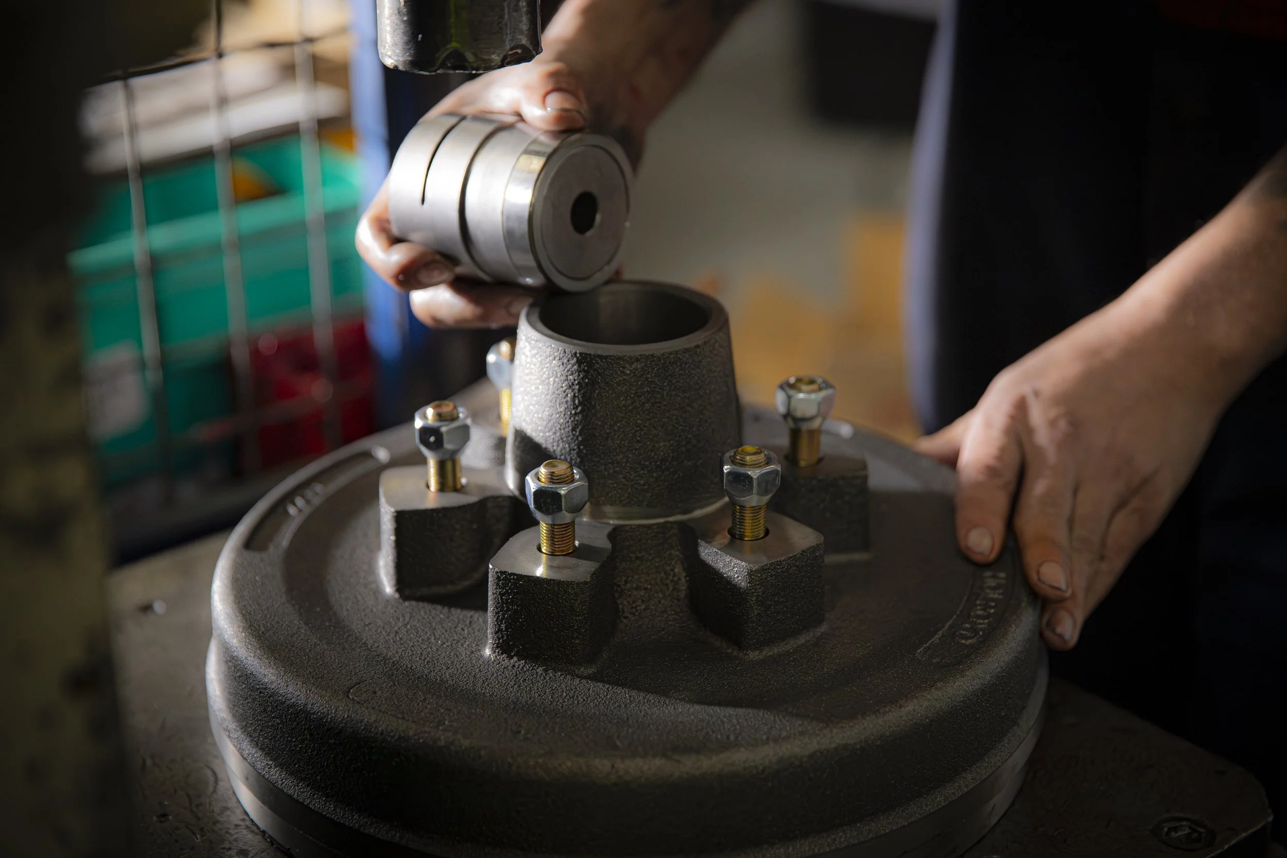 Close-up of a person working on a mechanical device, placing a metal part into a machine with multiple bolts and a textured surface.